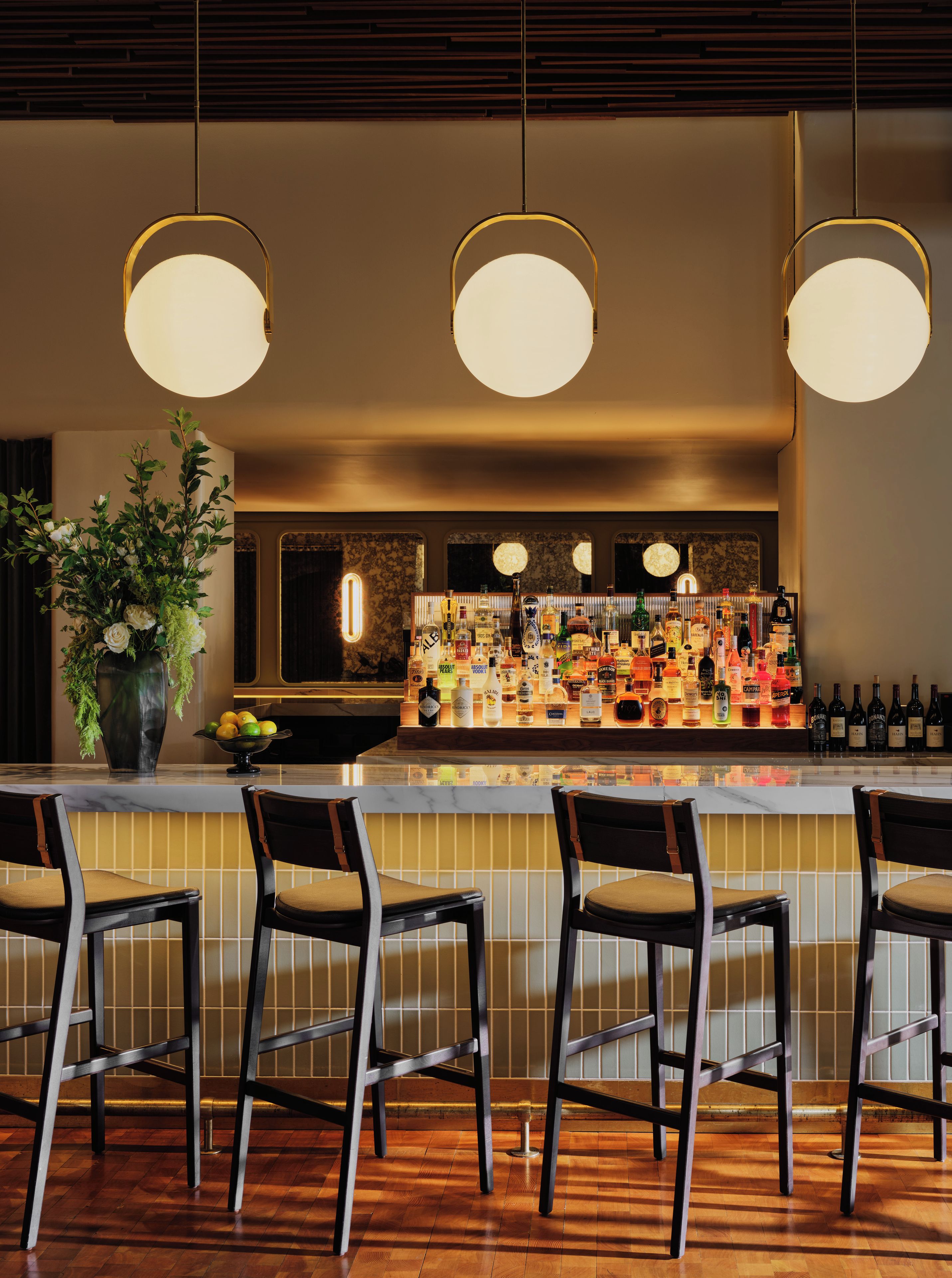 A bar area with a polished wooden floor, bar stools, and a well-stocked bar counter.