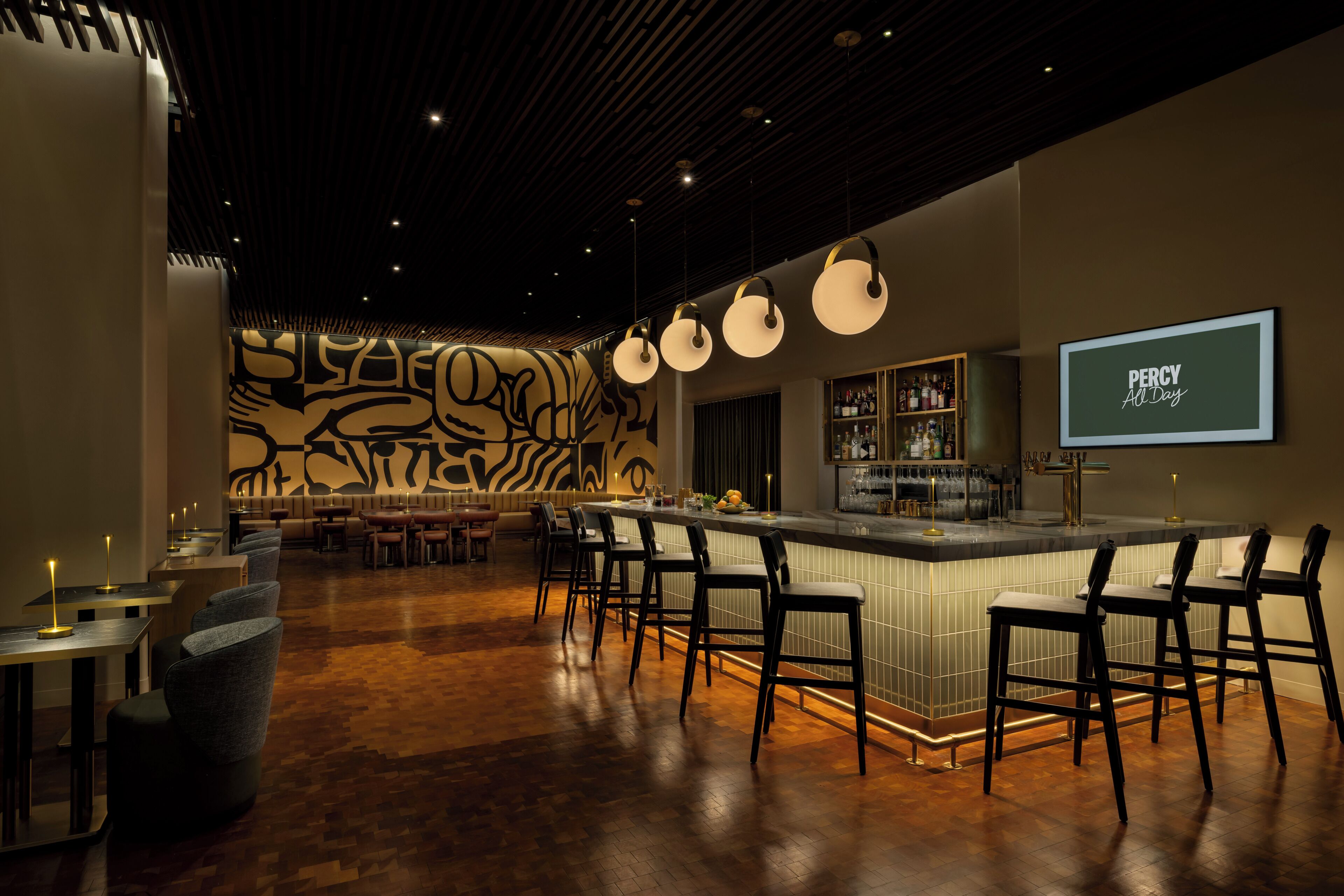 Zona de bar con mostrador, taburetes y un fondo de pared con diseño.