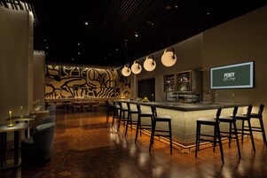 Eine Bar mit einer Theke, Hockern und einer gemusterten Wand im Hintergrund.