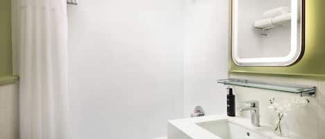 Un baño moderno con ducha, lavabo y estante de vidrio, además de un espejo.