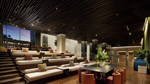 A modern lounge area with tiered seating, a central table, and a staircase leading to upper levels. - ROW NYC (New York)