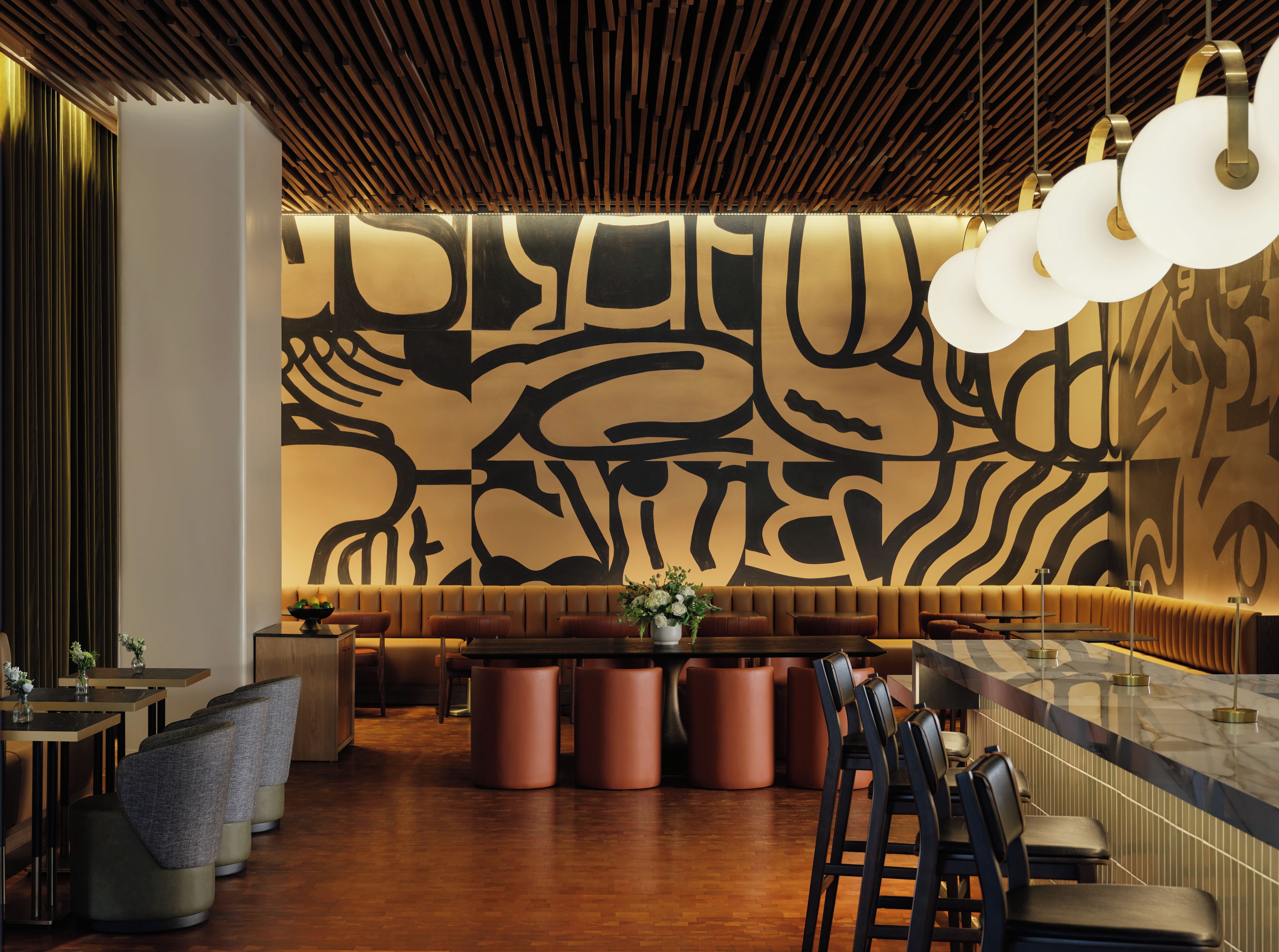 Un interior moderno con techo de madera, pared con diseño y zona de bar con taburetes y mesas.