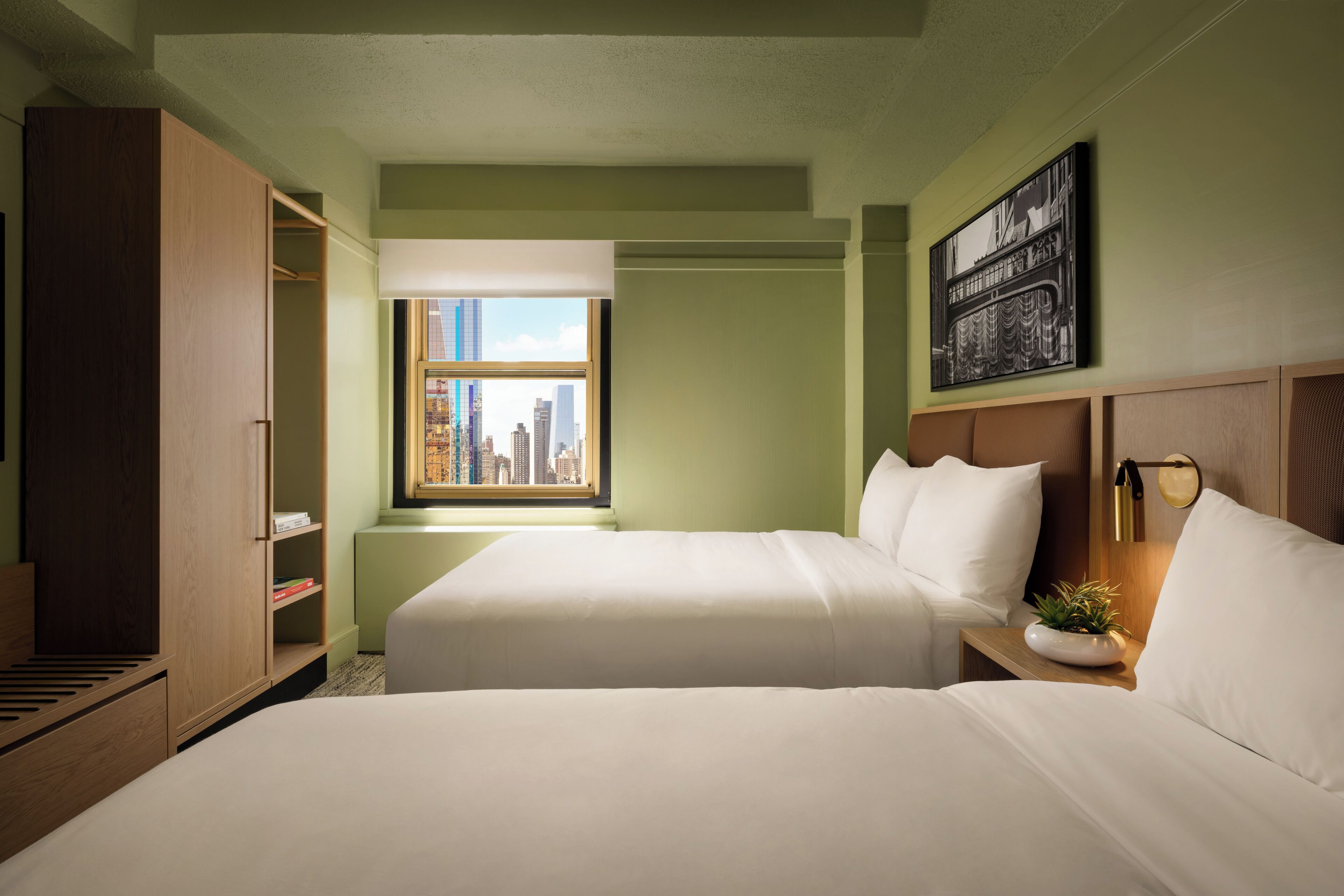 Habitación de hotel con dos camas, un armario, una ventana con vista a la ciudad y una obra de arte colgada en la pared.