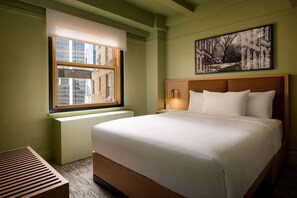 A hotel room with a large bed, a window with a view of buildings, a bedside table with a lamp, and a framed picture on the wall. - ROW NYC (New York)