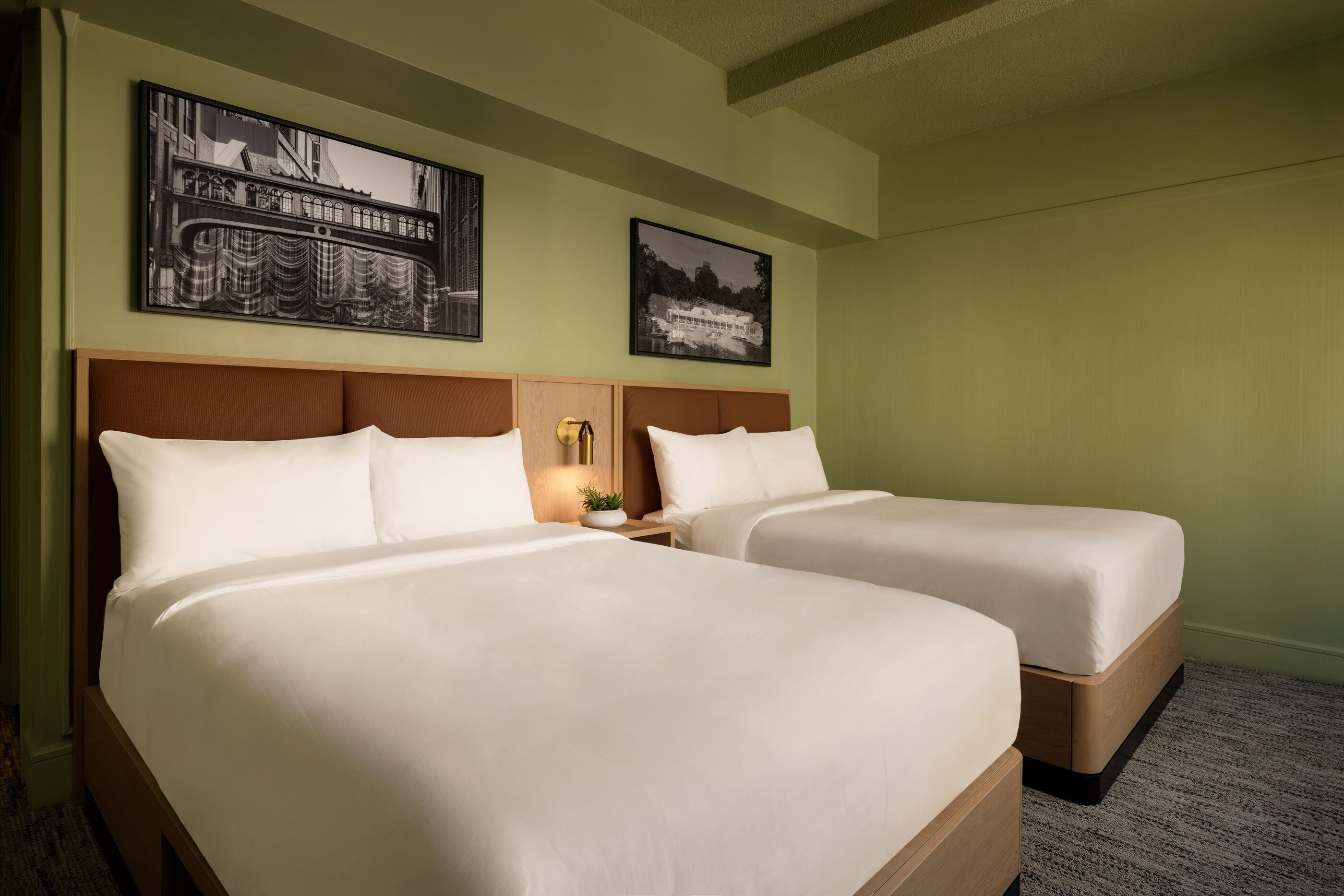 Ein Hotelzimmer mit zwei Betten, einem Nachttisch mit Lampe und zwei gerahmten Bildern an der Wand.