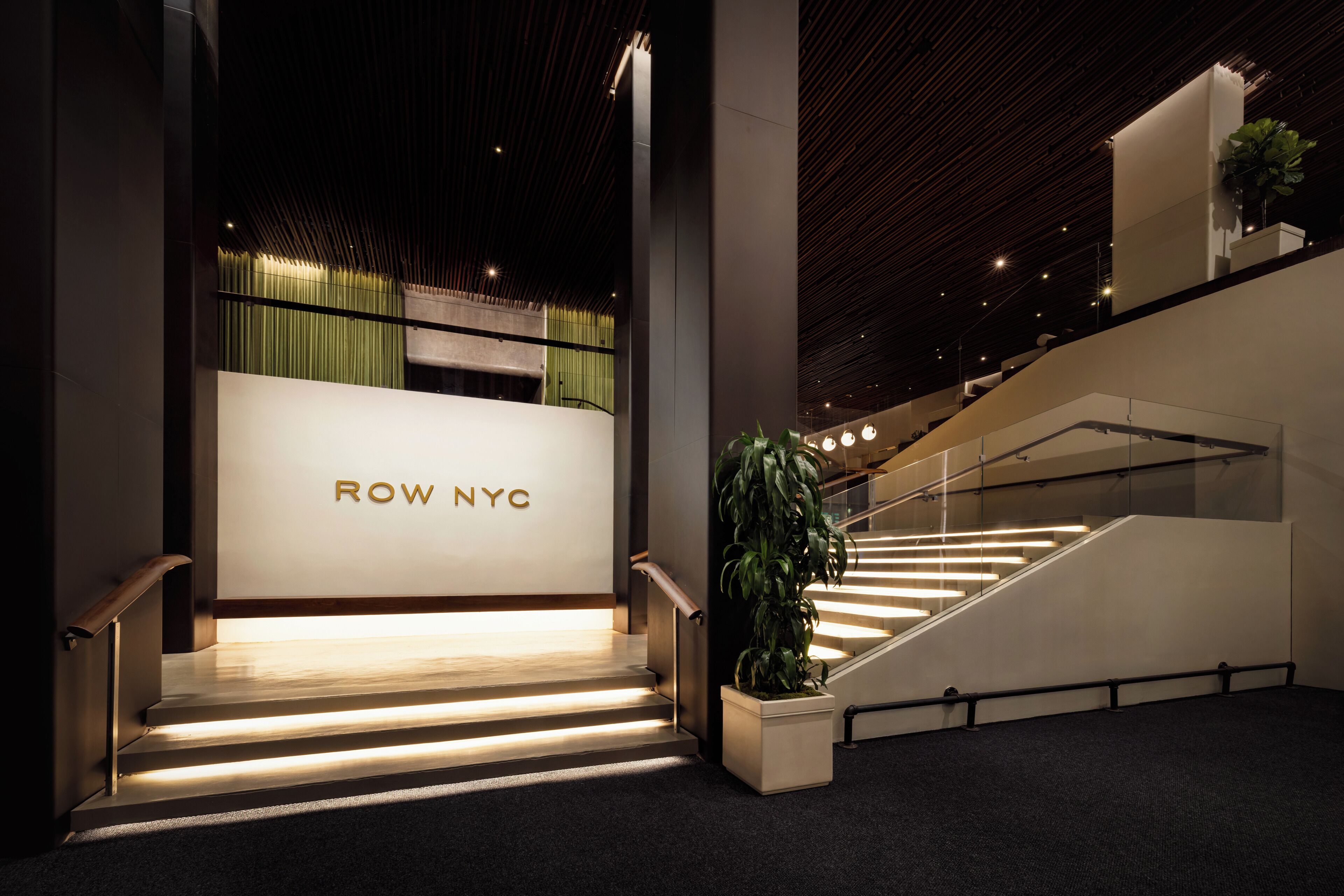 Un interior moderno con una escalera, un letrero que dice 'ROW NYC' y una planta en maceta.
