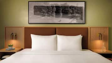 A bed with white linens, a headboard with wood paneling, two bedside tables with lamps, and a framed black-and-white photograph above the bed.