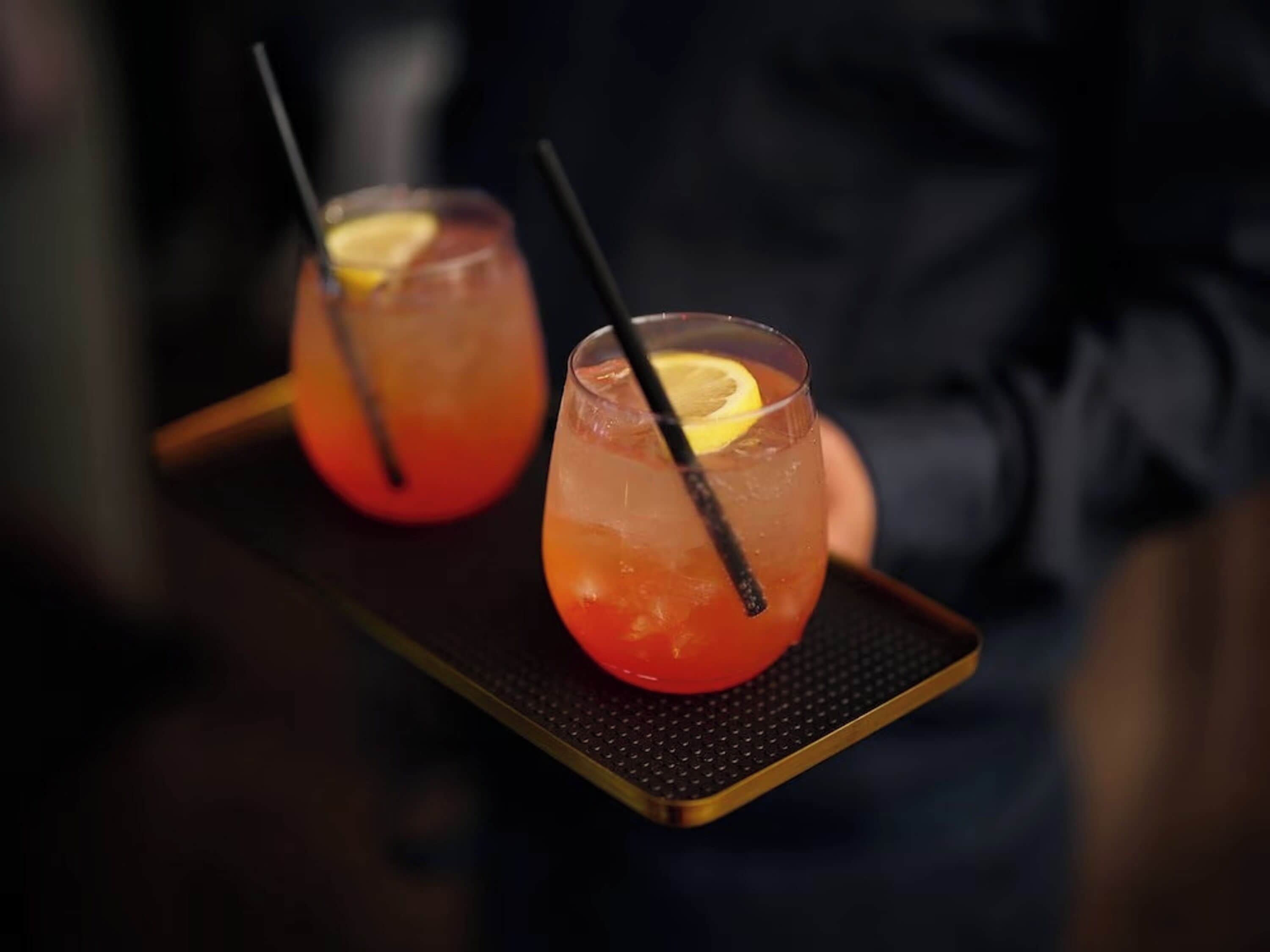 Two glasses of a red beverage with lemon slices on a tray.