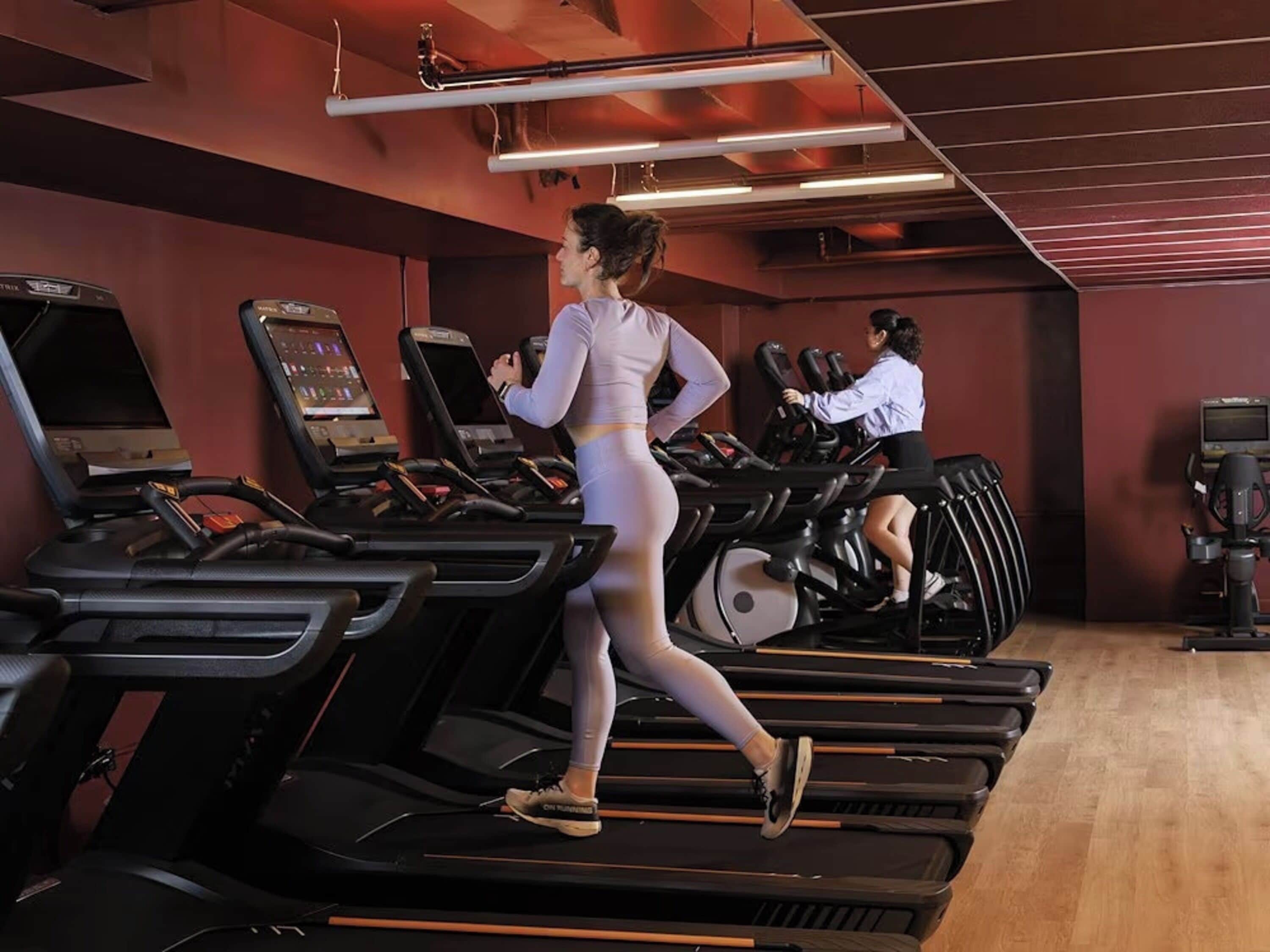 Un gimnasio con cintas de correr y elípticas, con dos personas haciendo ejercicio.