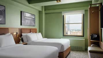 A hotel room with two beds, a large window with a city view, a wardrobe, and a framed picture on the wall.