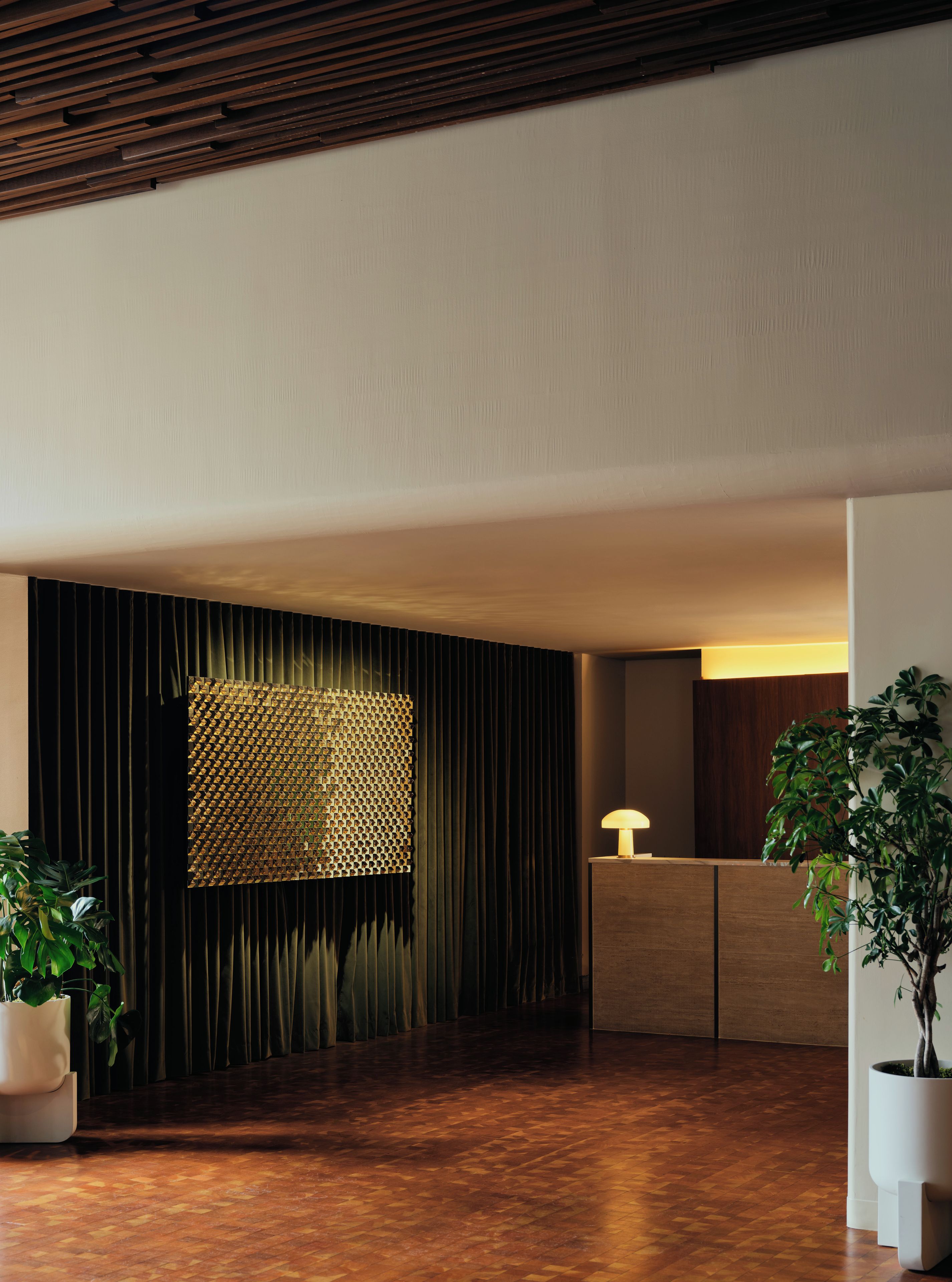 A reception area with a wooden reception desk, a patterned wall, and a potted plant.