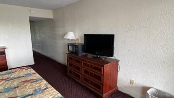 A hotel room with a bed, a wooden dresser, a television, and a lamp.