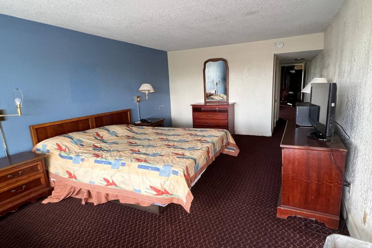 Ein Hotelzimmer mit einem großen Bett, einem Schminktisch, einem Fernseher und einem Spiegel.