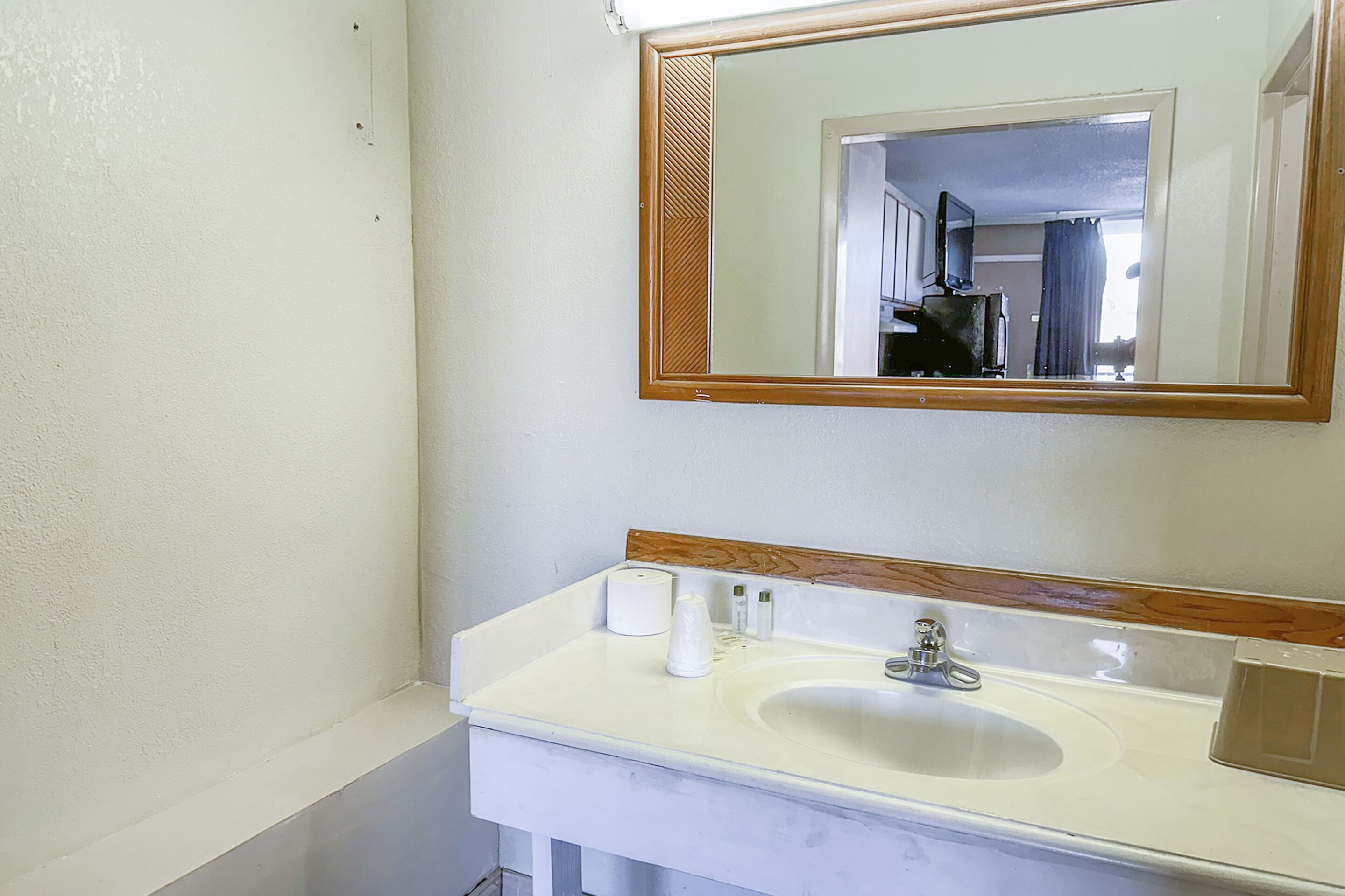 Un baño con un lavabo blanco, un espejo con marco de madera y un inodoro visible en el reflejo.