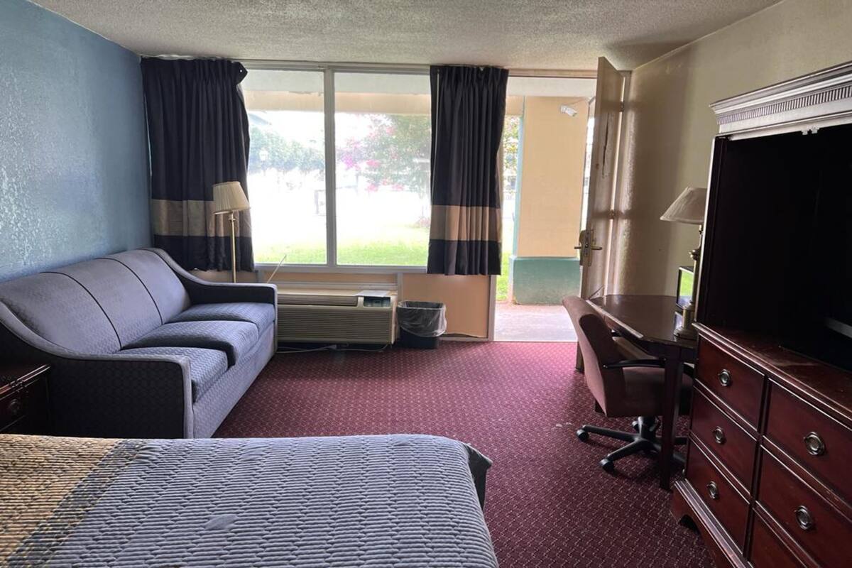 Ein Hotelzimmer mit Bett, Sofa, Schreibtisch und Fernseher sowie einem Fenster mit Vorhängen.