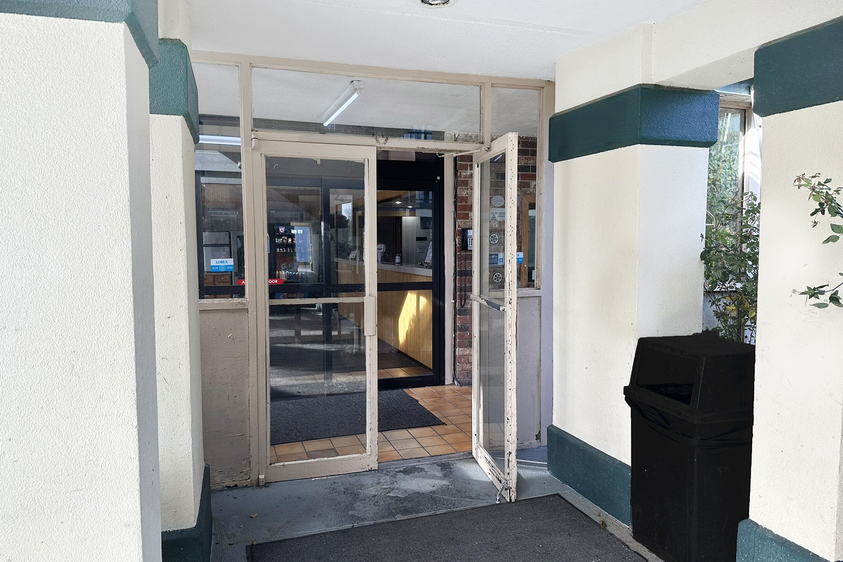 Entrada d'hotel amb una porta de vidre, un safataire i una zona interior petita amb un taulell i seients.