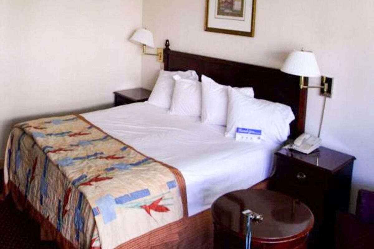 Ein Hotelzimmer mit Bett, Nachttisch, Lampe und Koffer.