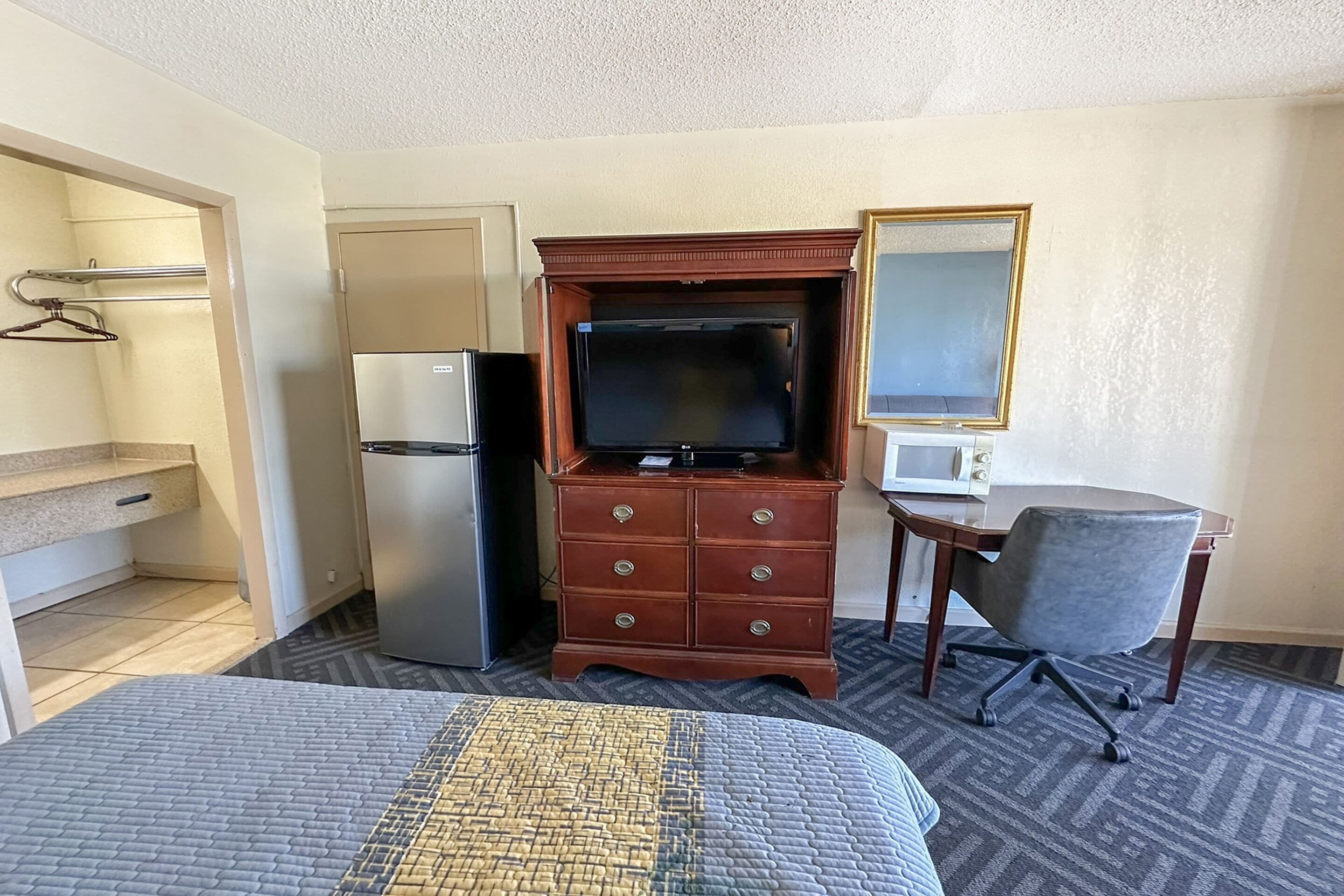 Habitación de hotel con cama, cómoda, televisor, refrigerador, microondas, silla y escritorio.