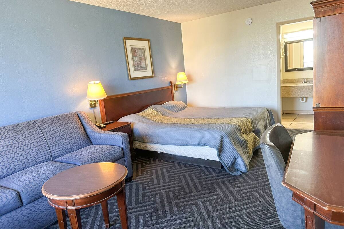 Ein Hotelzimmer mit einer Couch, zwei Einzelbetten, einem kleinen Tisch und einem Nachttisch aus Holz mit Lampen.
