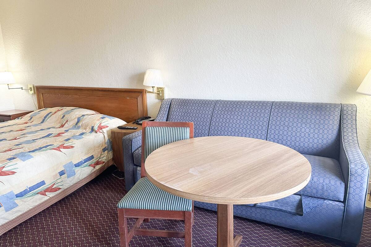 Ein Hotelzimmer mit einem Bett, einem runden Holztisch, einem blauen Sofa und gestreiften Stühlen.