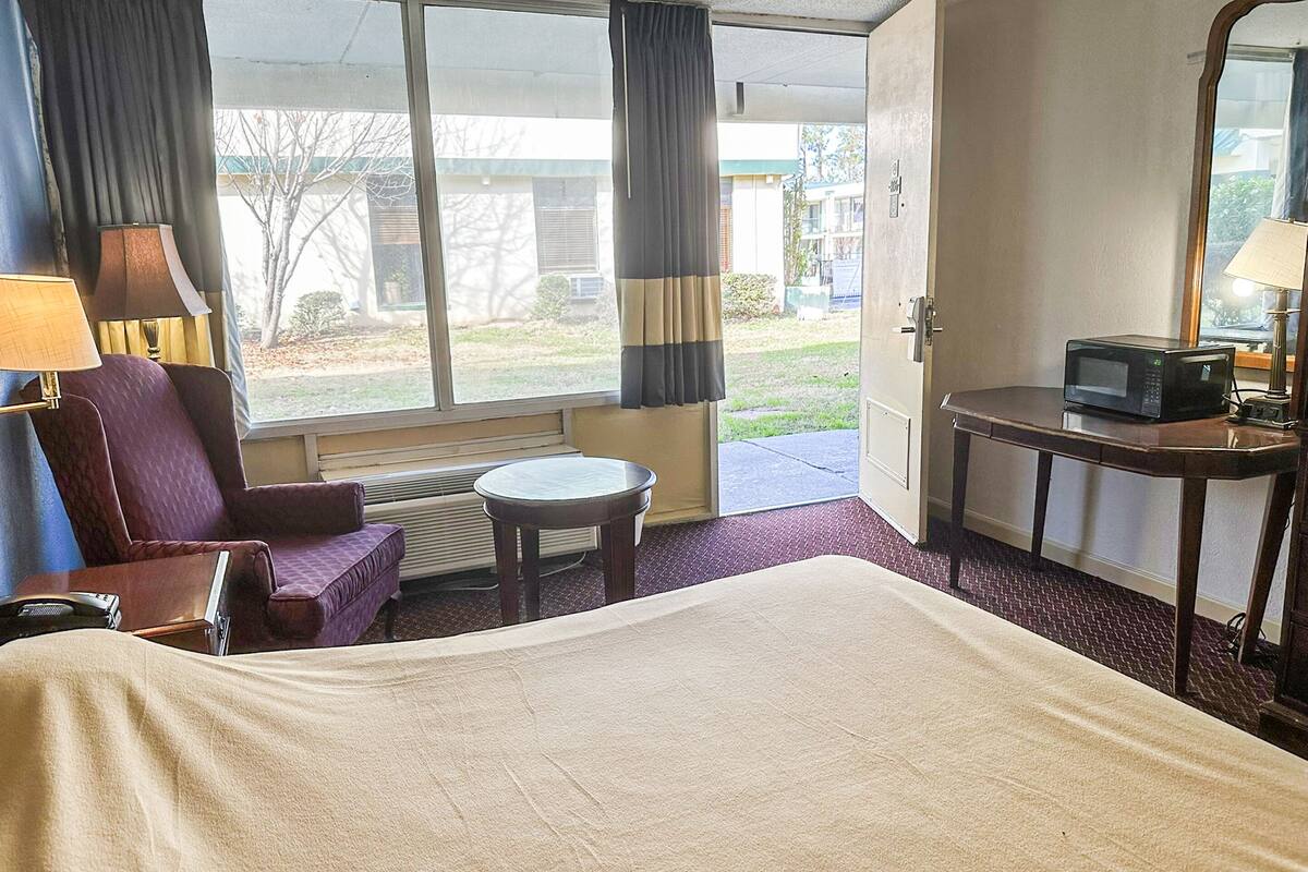 Ein Hotelzimmer mit Bett, Sessel, kleinem Tisch, Mikrowelle und einem Fenster mit Vorhängen.