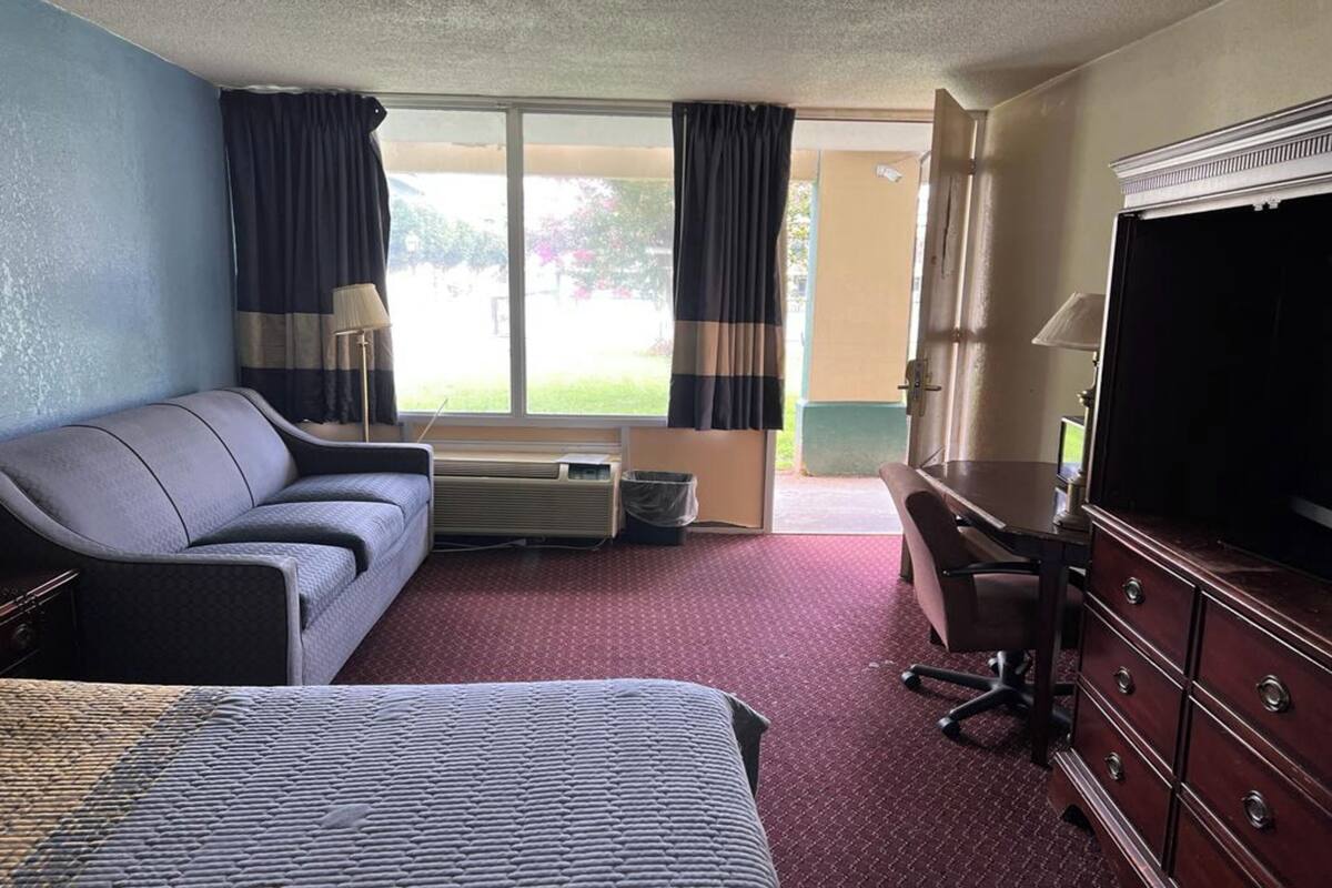 Ein Hotelzimmer mit Bett, Sofa, Schreibtisch und Fernseher sowie einem Fenster mit Vorhängen.