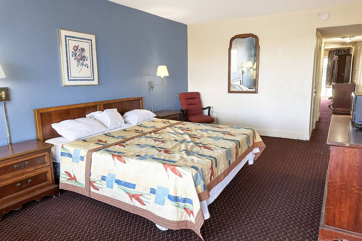 Ein Hotelzimmer mit einem Bett, einem Sessel, einem Schminktisch und einem Bild an der Wand.