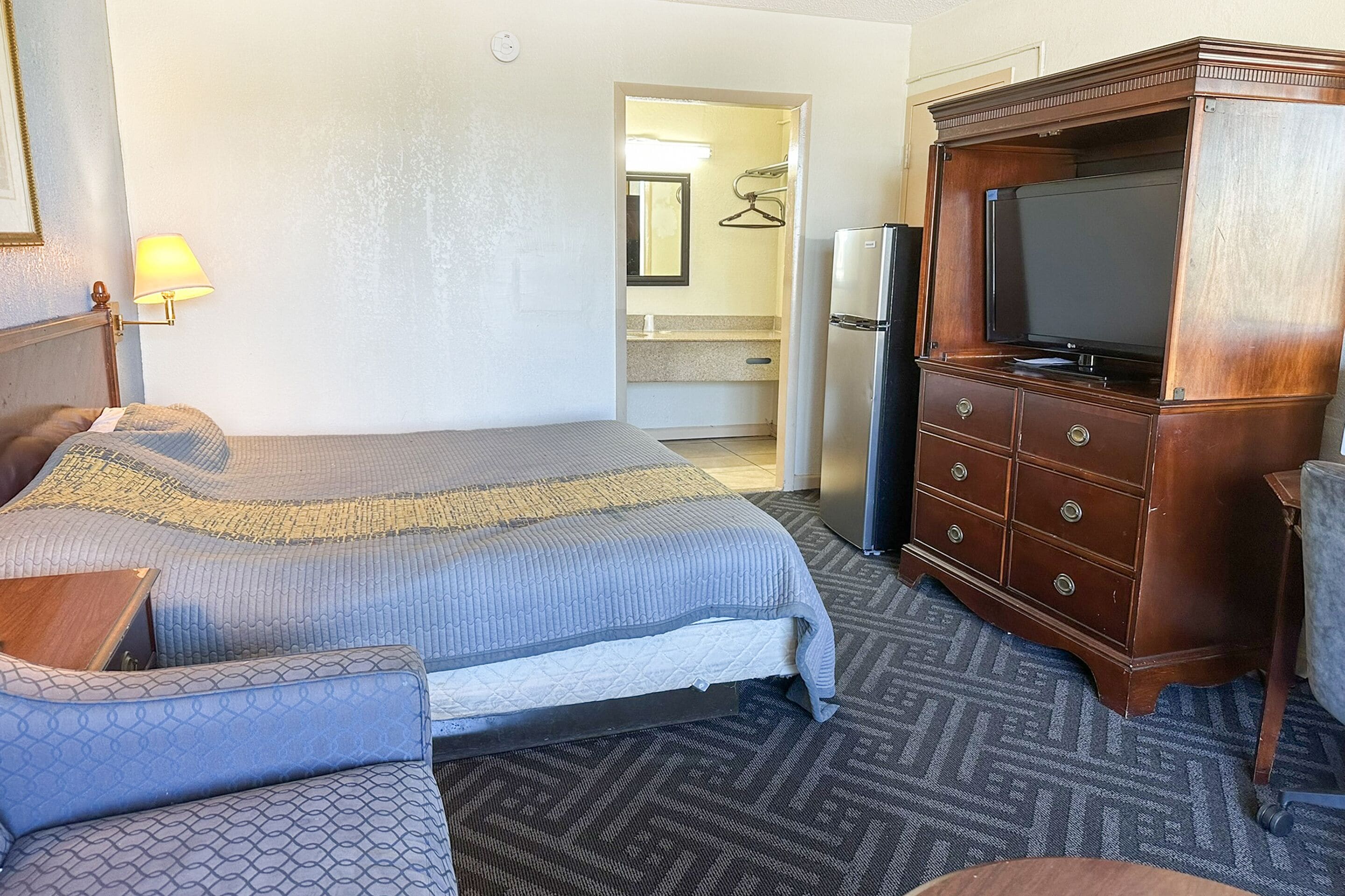 Una habitación de hotel con cama, cómoda, televisión y baño visible a través de una puerta abierta.