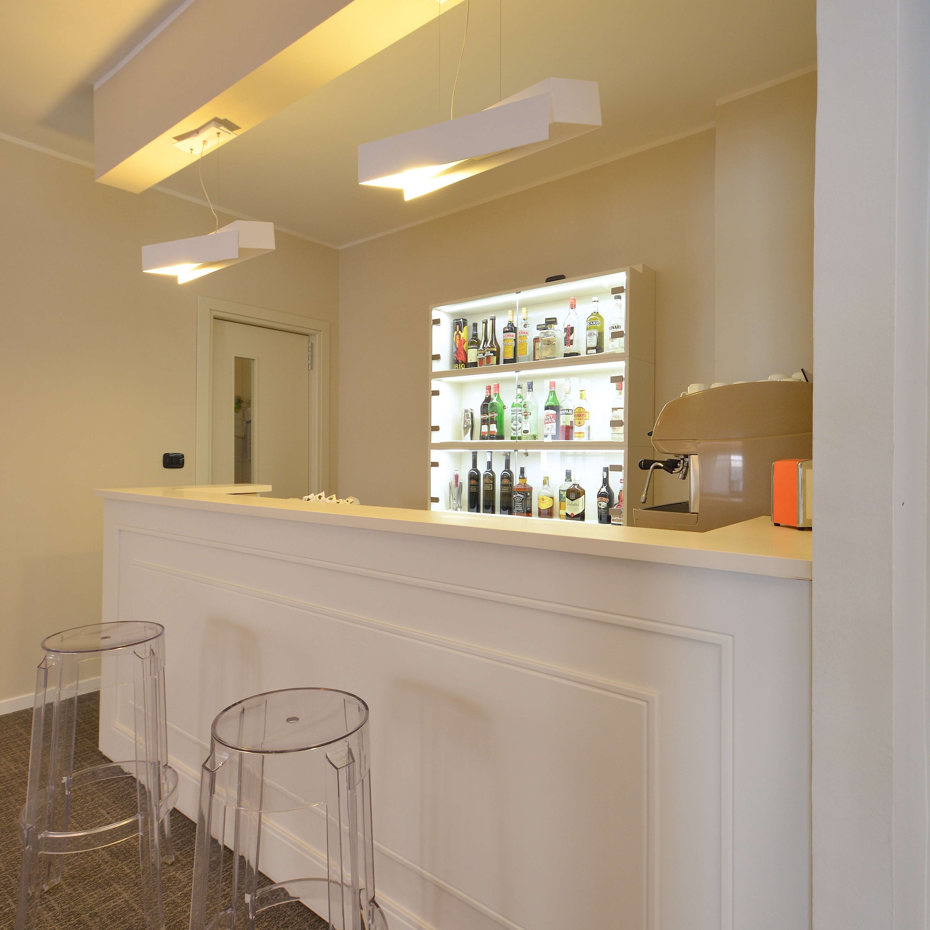 Uma área de bar com balcão branco, prateleiras cheias de garrafas de bebidas e uma máquina de café.