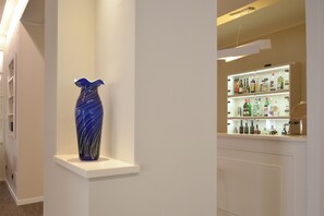 Un couloir avec un vase bleu posé sur une étagère blanche et un coin bar où sont exposées différentes bouteilles d’alcool.