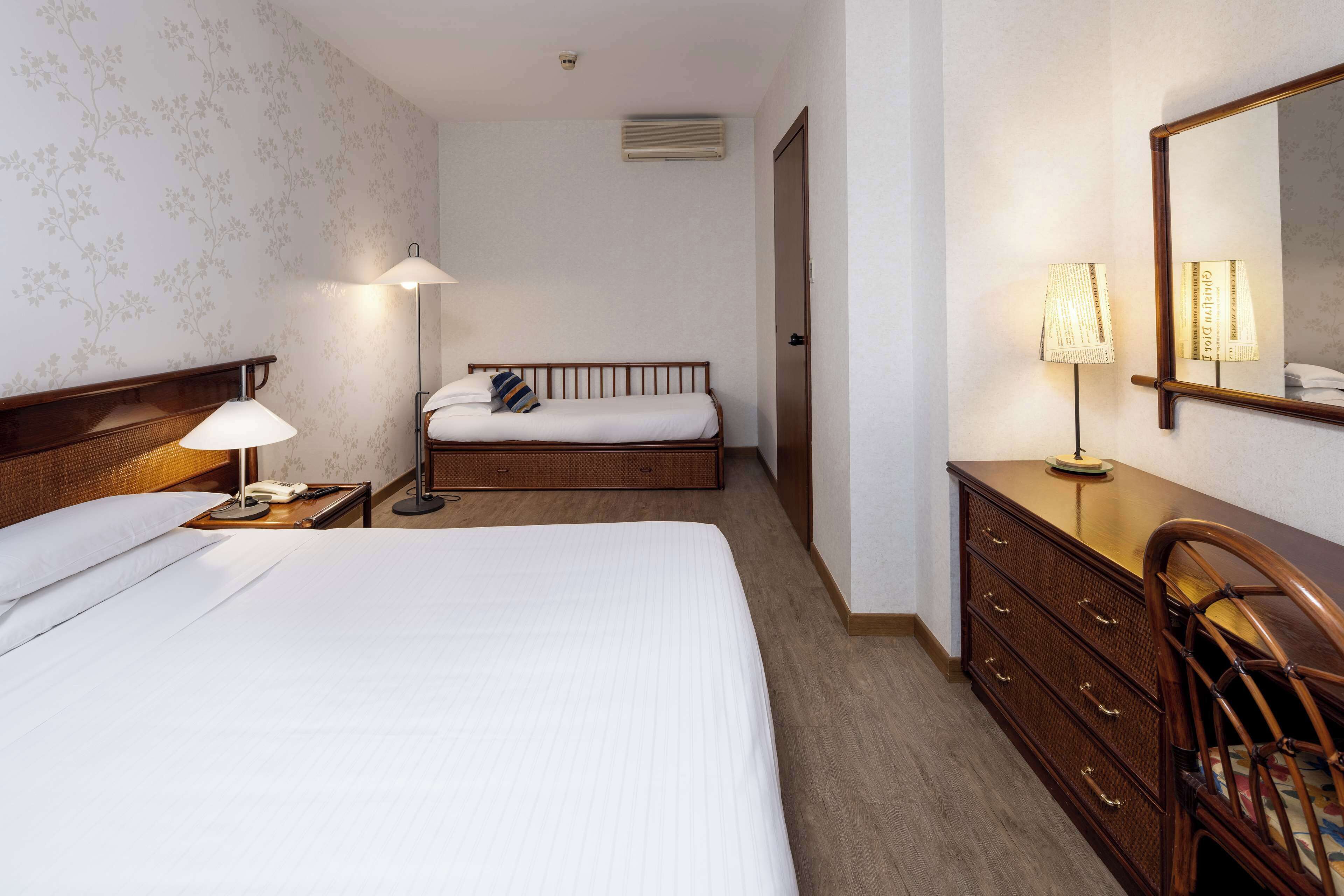 A hotel room with a large bed, a bedside table with a lamp, a dresser, and a mirror.