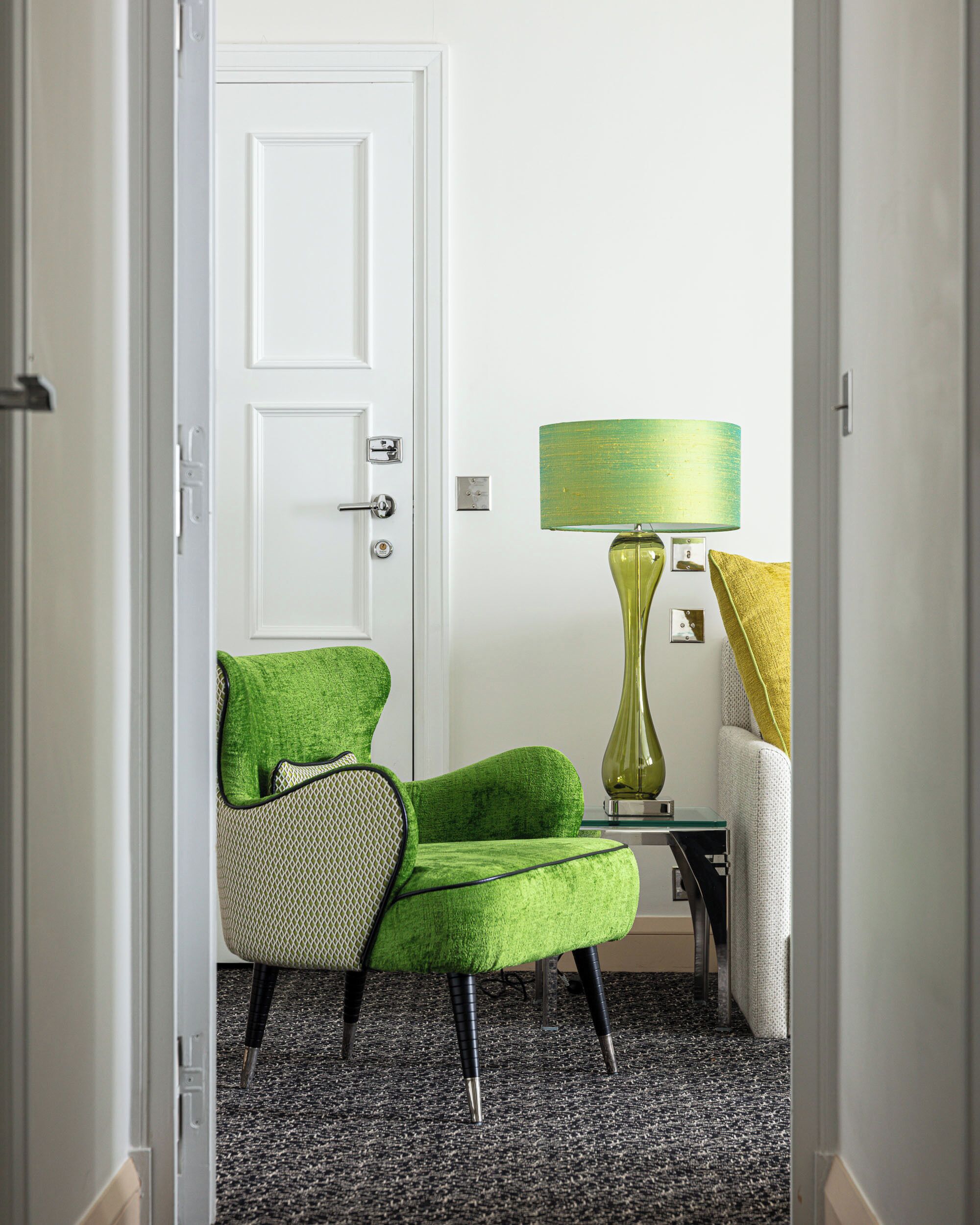 Un pasillo con un sillón verde, una lámpara y una puerta.