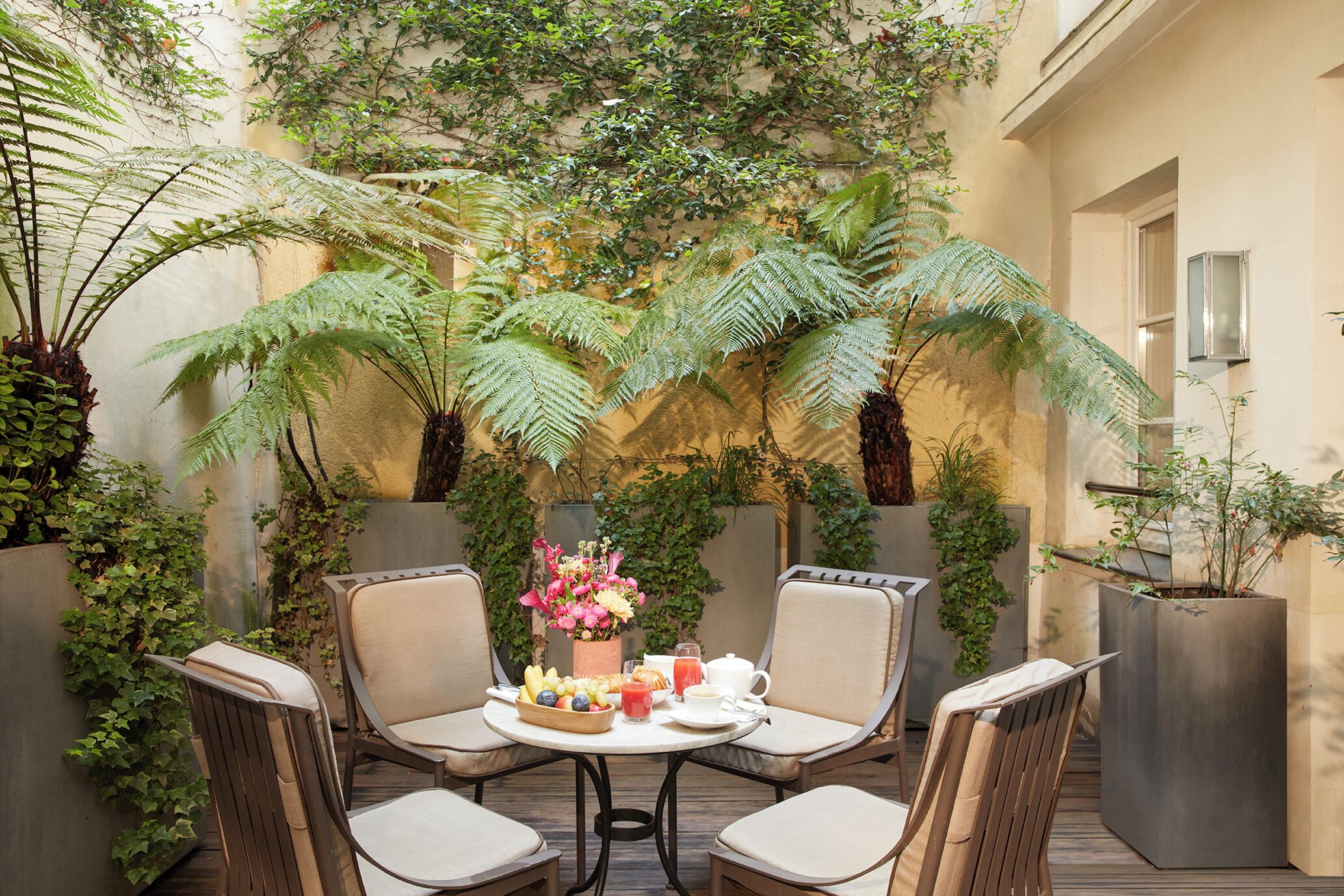 Un espace extérieur accueillant, aménagé avec une table ronde, quatre chaises et une variété de plantes et de fleurs.