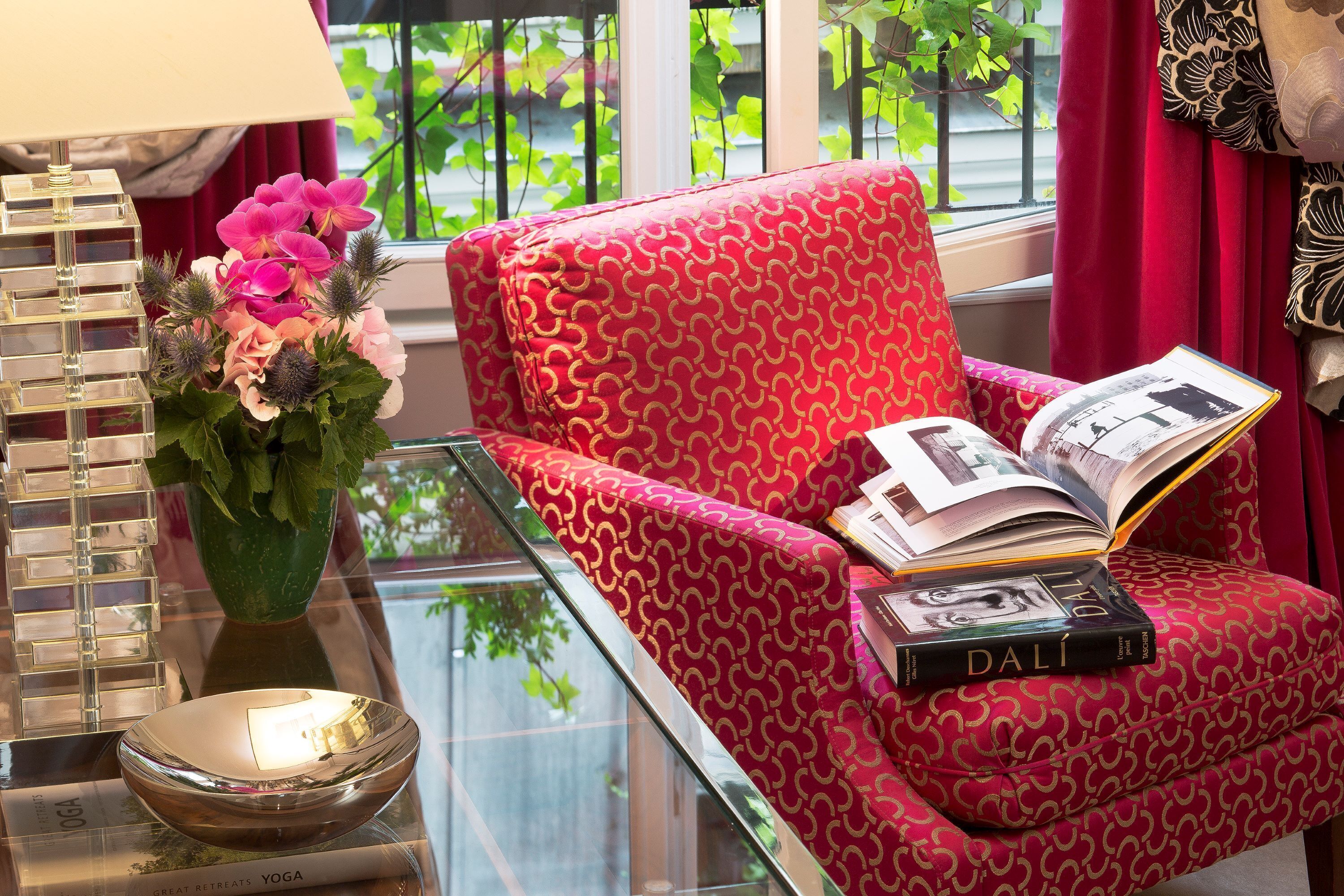 Un fauteuil rouge à motifs, avec un livre et un vase de fleurs posés sur une table en verre.