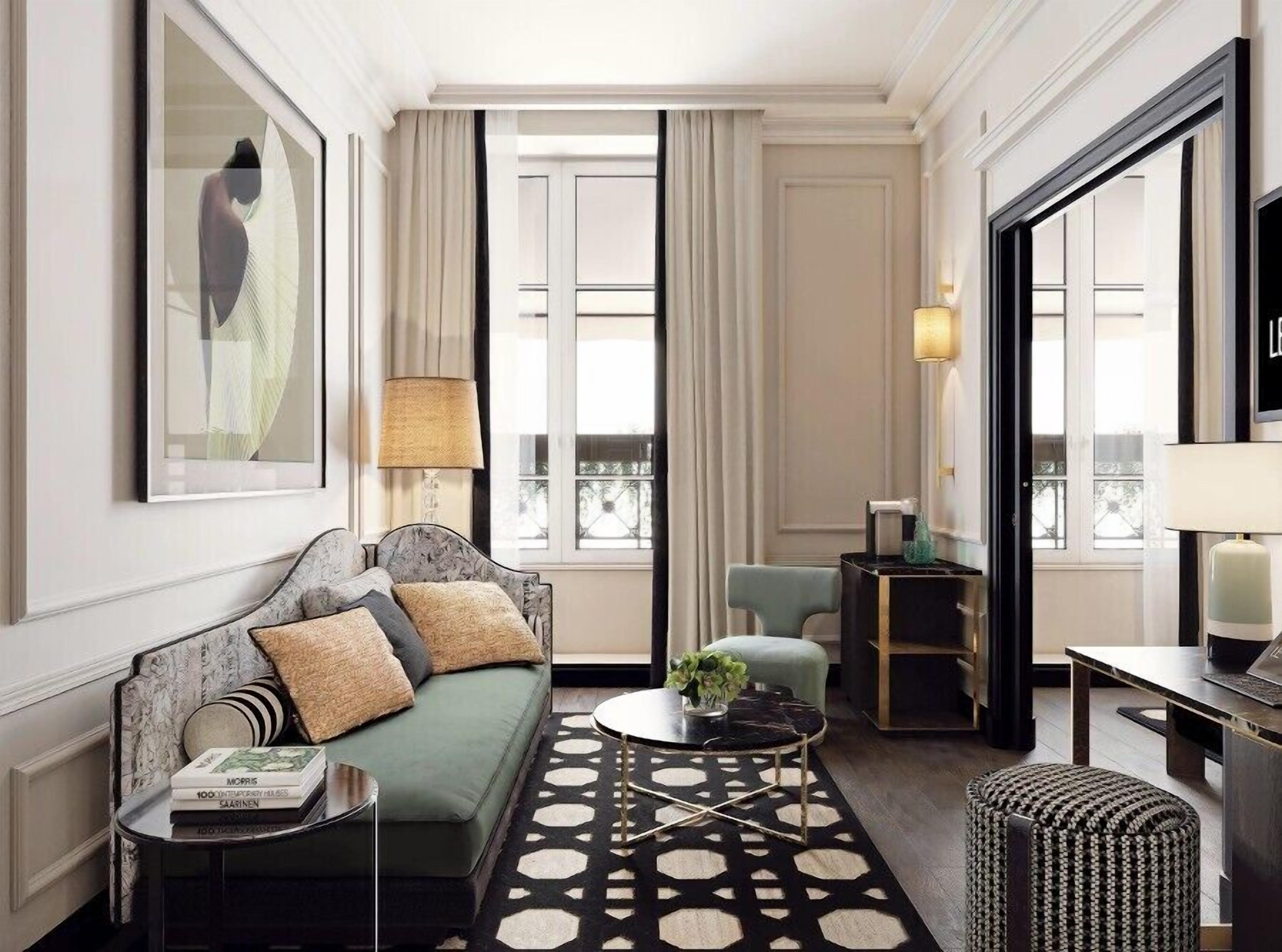 Une chambre d’hôtel moderne avec un canapé vert, une table basse ronde, une table d’appoint avec des livres, une petite table d’appoint avec une lampe et une grande fenêtre avec des rideaux.
