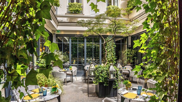 An outdoor café area with round tables and chairs, surrounded by greenery and plants. - Le Burgundy Paris (Paris)