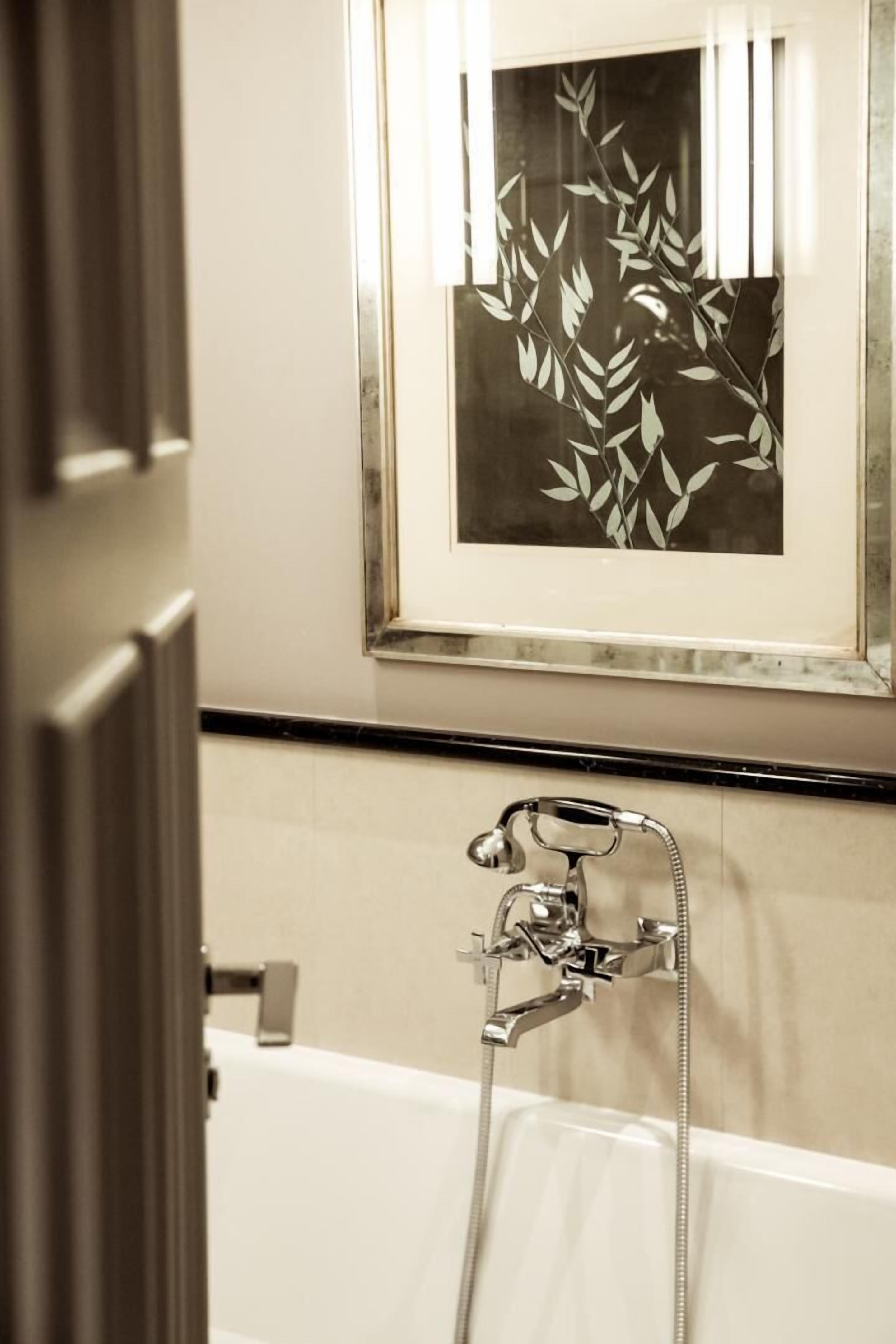 Un baño con una obra de arte enmarcadas de hojas, una bañera y una ducha con cabezal de ducha manual.