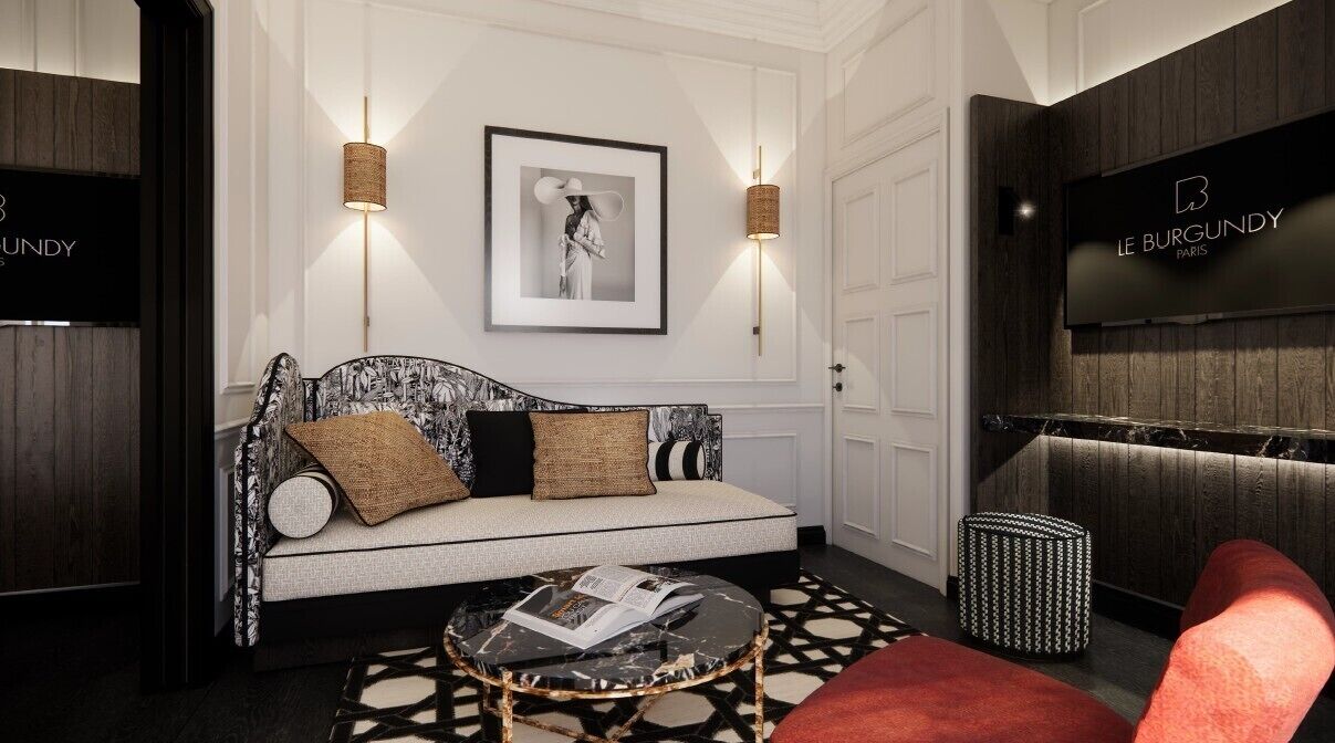Un salon moderne avec un canapé, une table basse ronde et un fauteuil rouge. Un tableau encadré est accroché au mur, et une enseigne indique « LE BURGUNDY PARIS ».