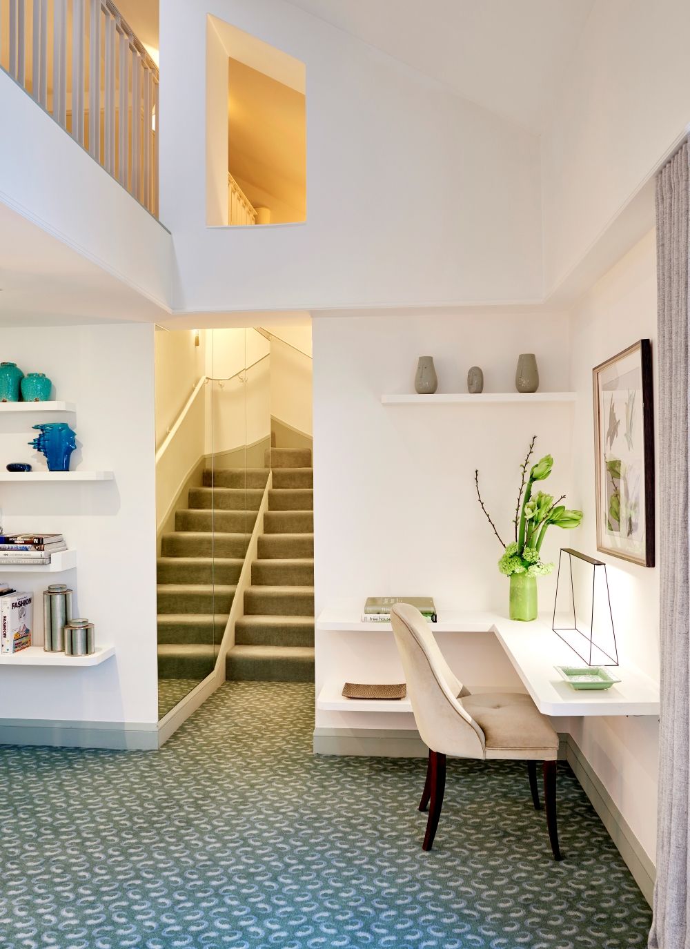 Un intérieur moderne avec un escalier, des étagères blanches, un bureau et un tapis à motifs.