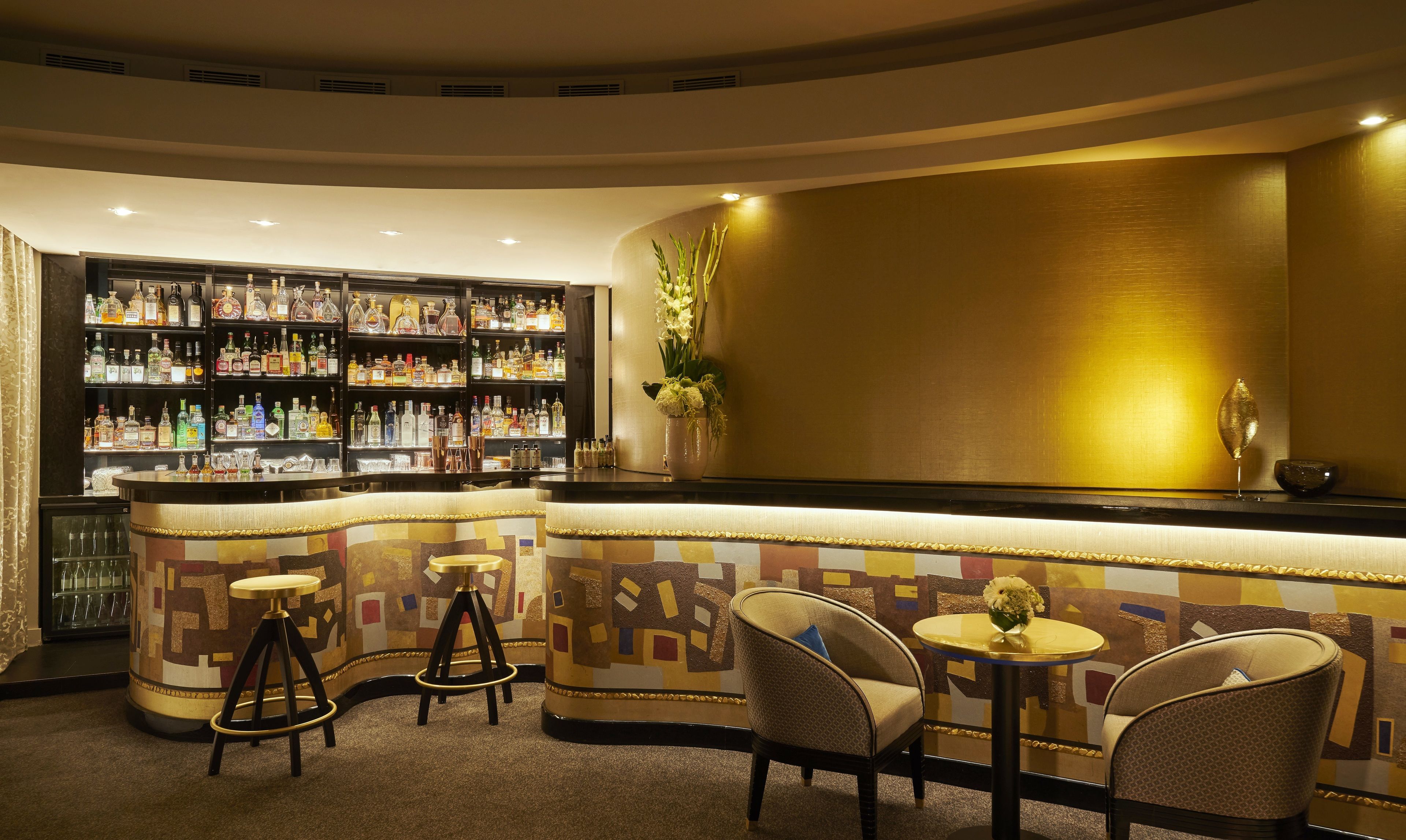 A bar area with a variety of liquor bottles, a bar counter, and seating with stools and chairs.