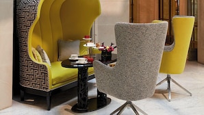 A modern lounge area with a yellow sofa, a grey armchair, and a small round table with a teapot and cups. - Le Burgundy Paris (Paris)