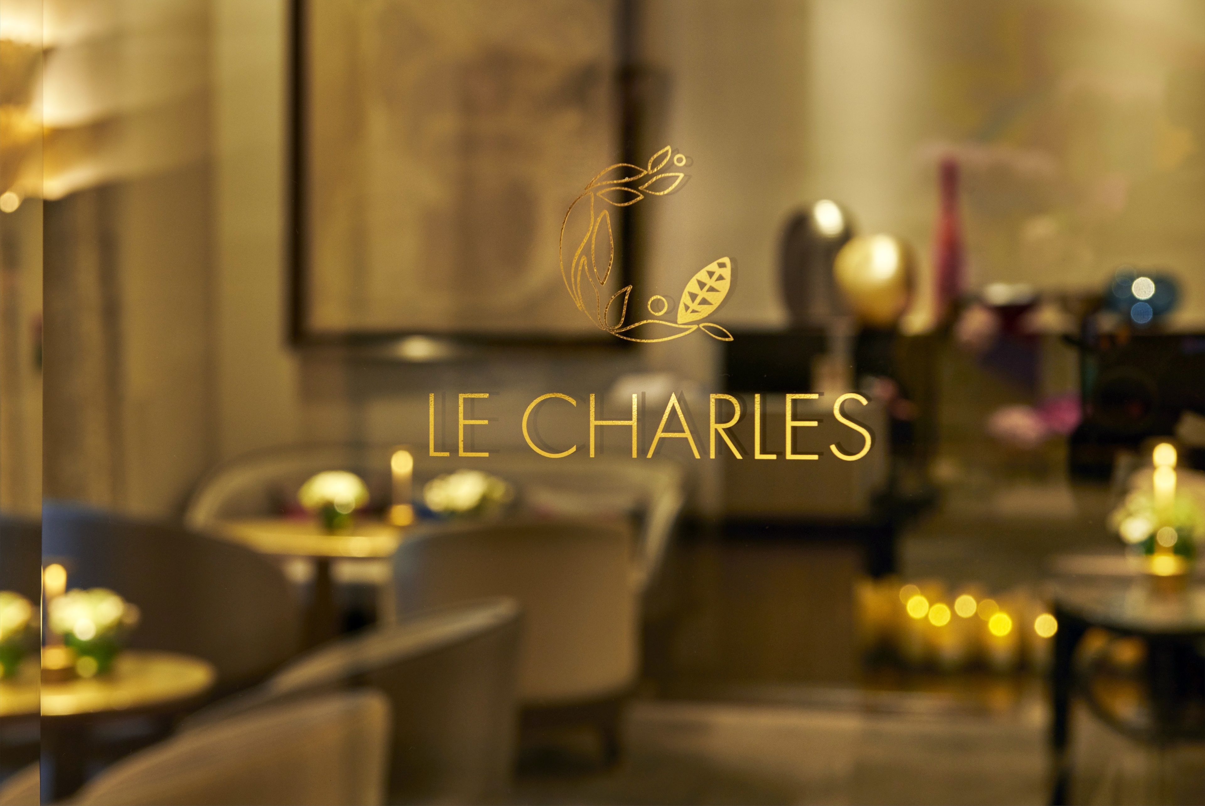 Ein unscharfes Innenbild eines Restaurants mit Tischen und Stühlen, wobei der Name "LE CHARLES" gut sichtbar ist.