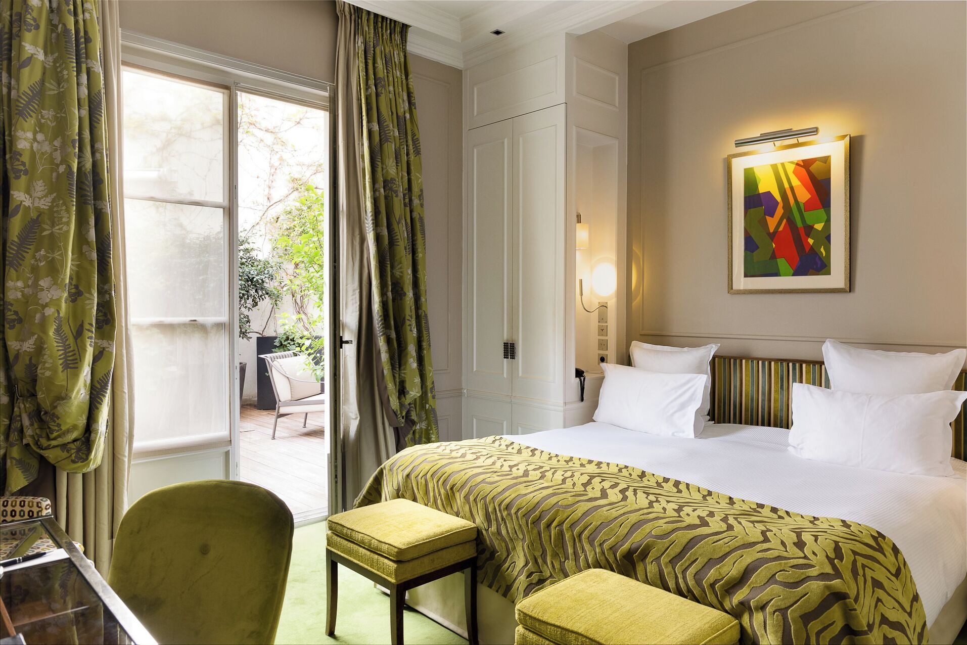 A hotel room with a bed, a chair, a desk, and a view of the outdoors.