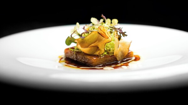 A white plate with a gourmet dish featuring a piece of meat, greens, and a sauce. - Le Burgundy Paris (Paris)