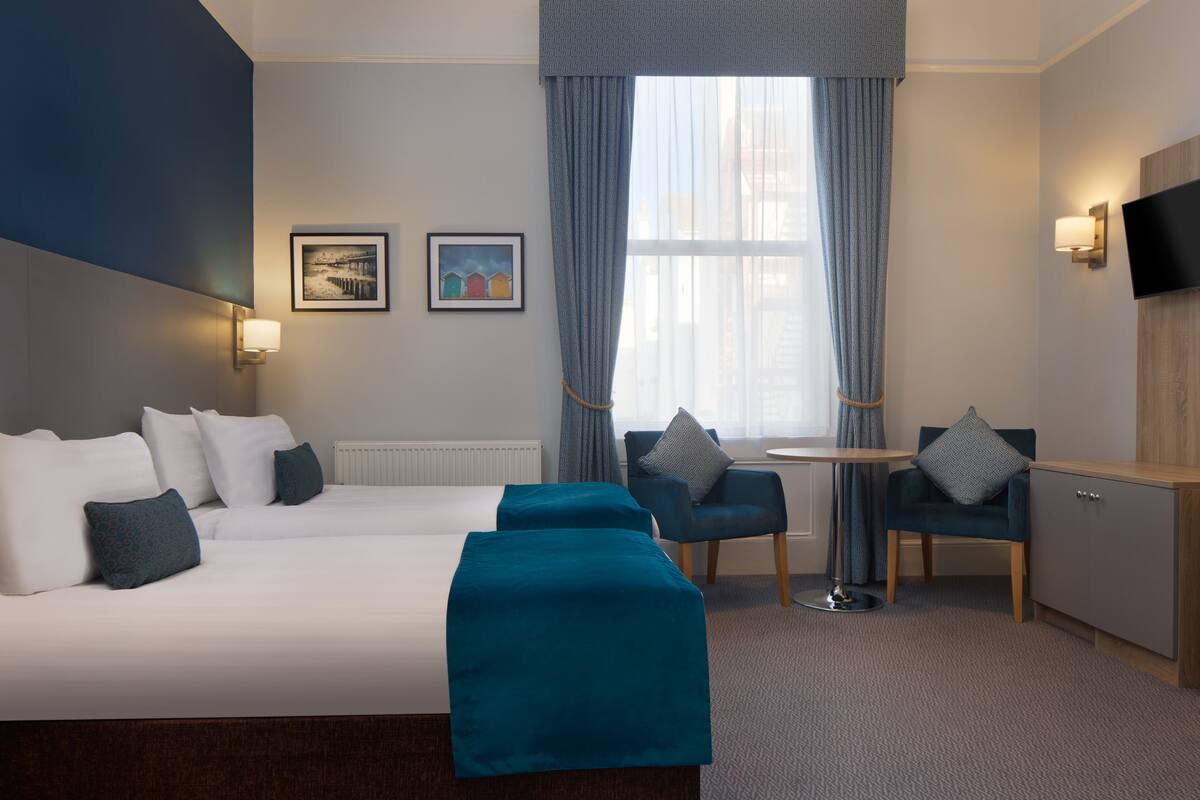 Habitación de hotel con una cama grande, dos sillones, una mesita y un televisor montado en la pared.