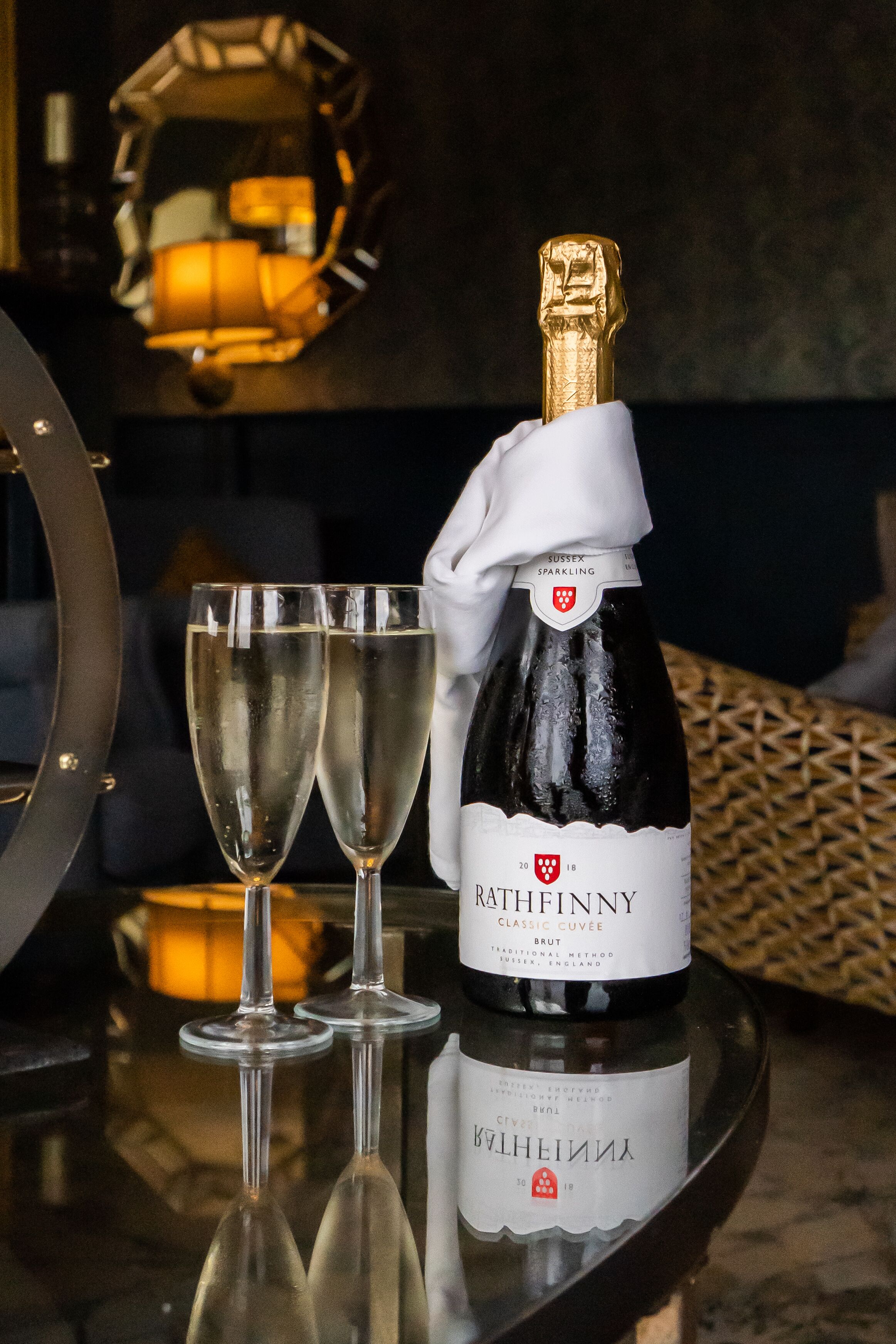A bottle of Ratthof Finny Classic Cuvee Brut on a reflective surface with two champagne flutes.