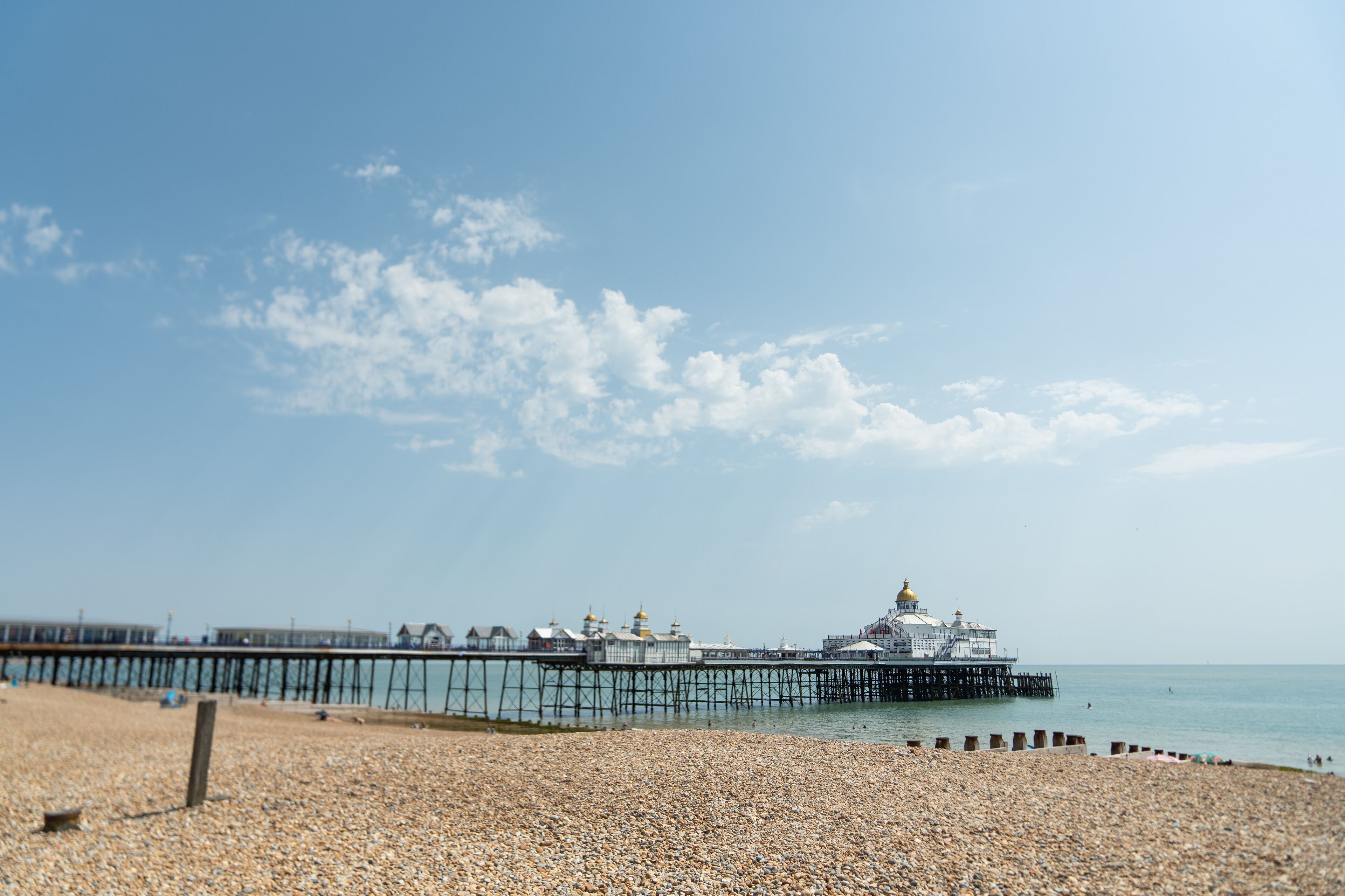 A pebbled beach with a pier extending into the water, featuring a large building with domed roofs.