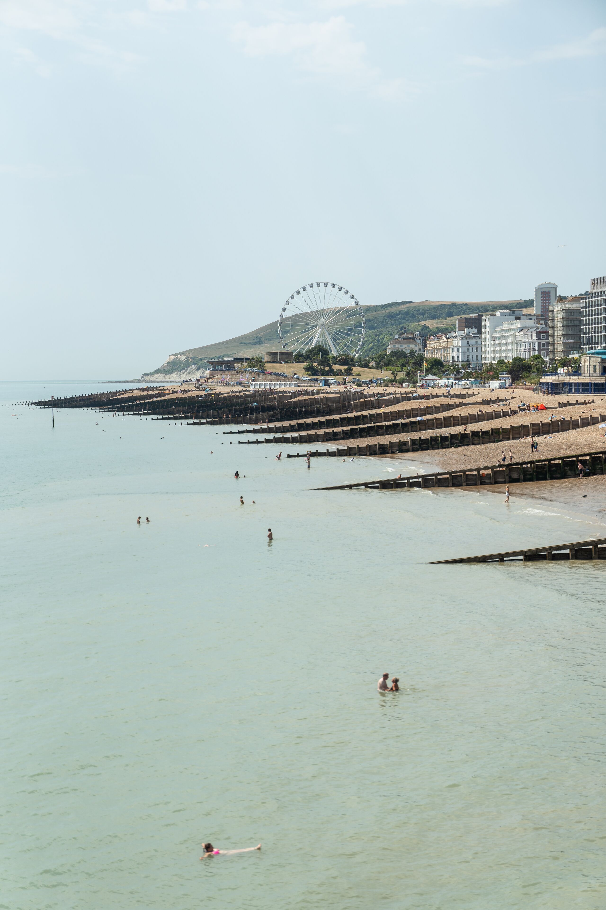 A beach with a Ferris wheel in the background, a pier extending into the water, and buildings nearby.