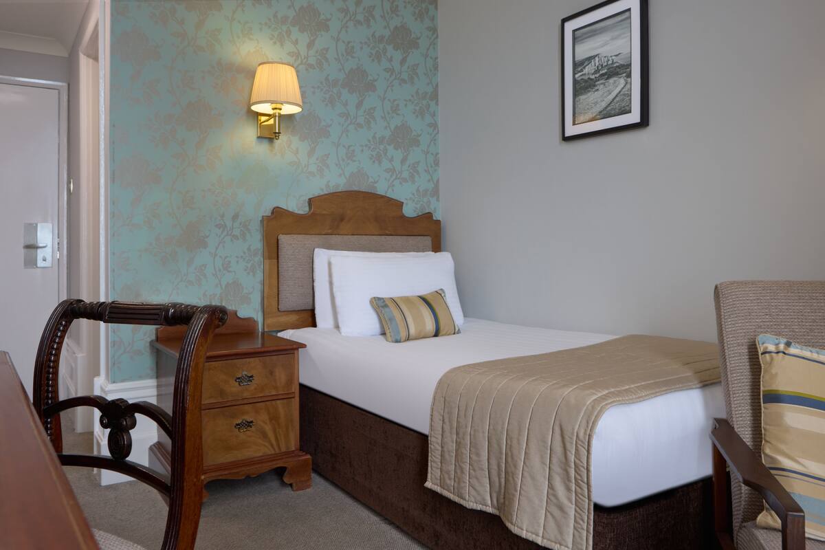 Una habitación de hotel con una cama, una mesita de noche, una lámpara y un cuadro en la pared.