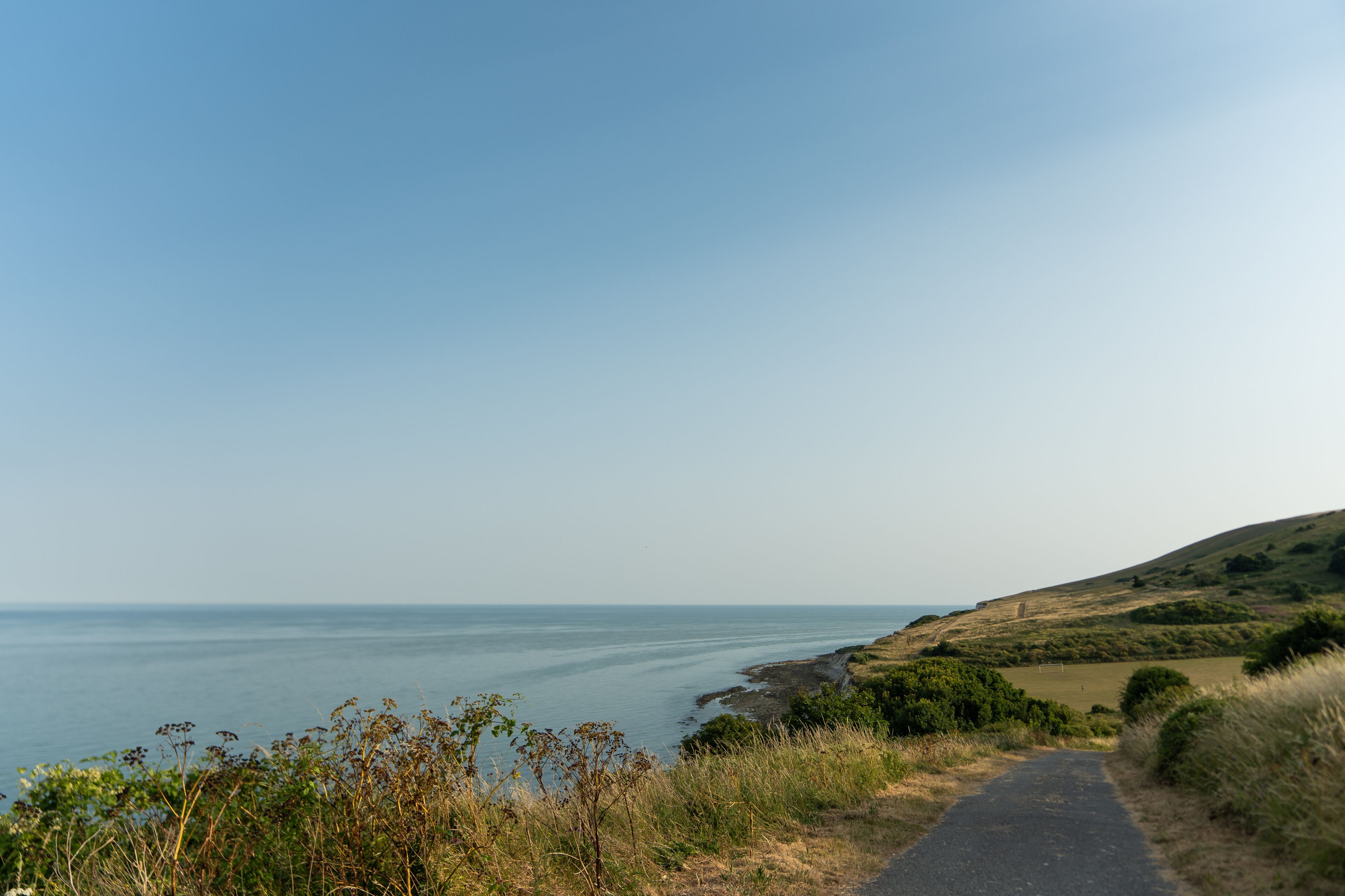 A coastal road with a clear view of the sea and a grassy hillside.